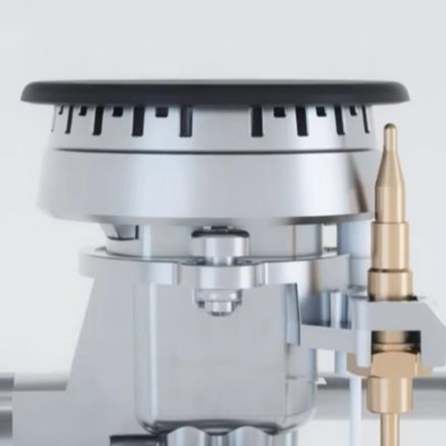 Un primo piano di un componente del bruciatore del fornello a gas. Mostra una base in metallo argentato con una parte superiore nera e un tubo color oro. Lo sfondo è bianco.