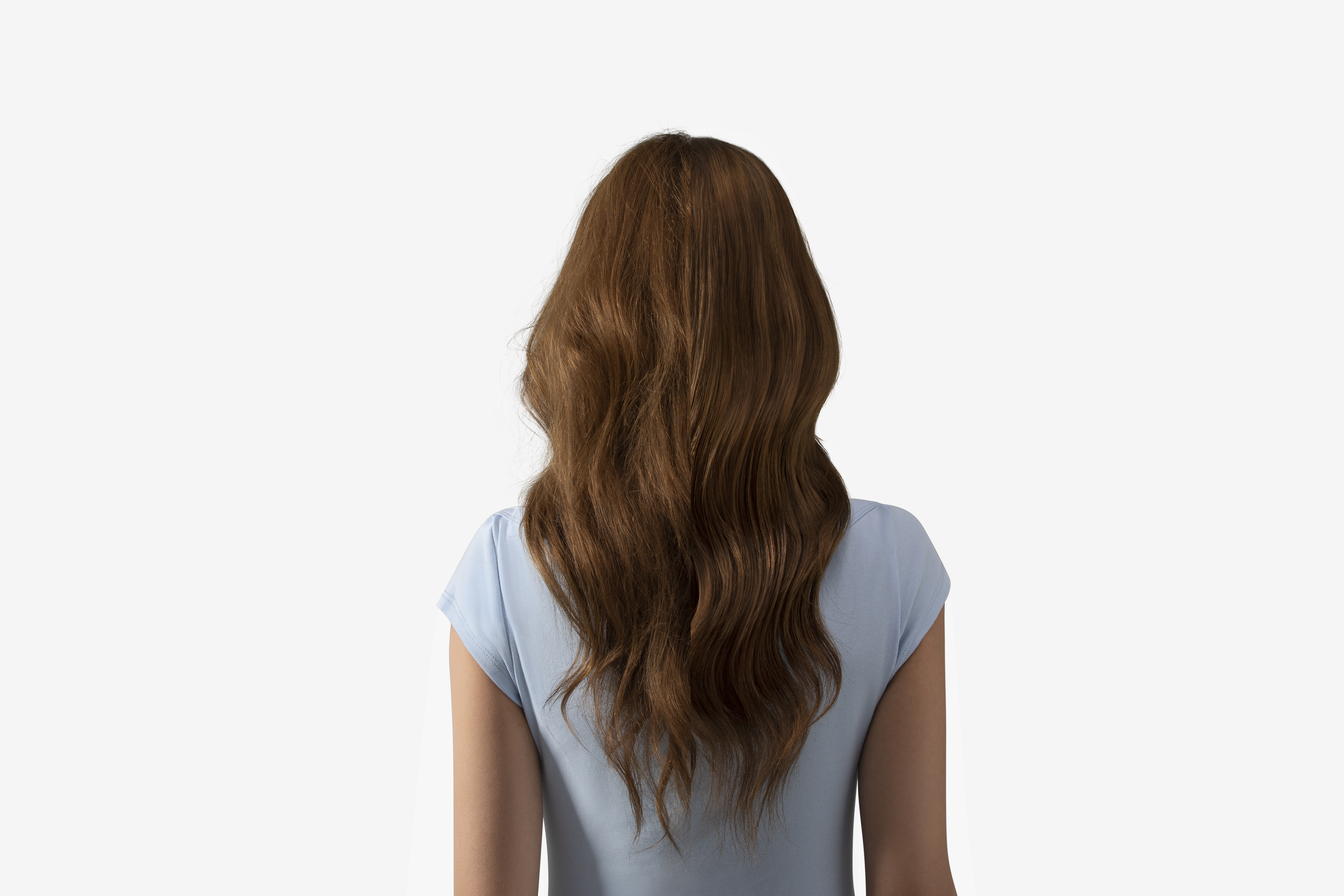 Kobieta od tyłu. Długie, falowane, kasztanowe włosy opadają na jasnoniebieski top, białe tło.