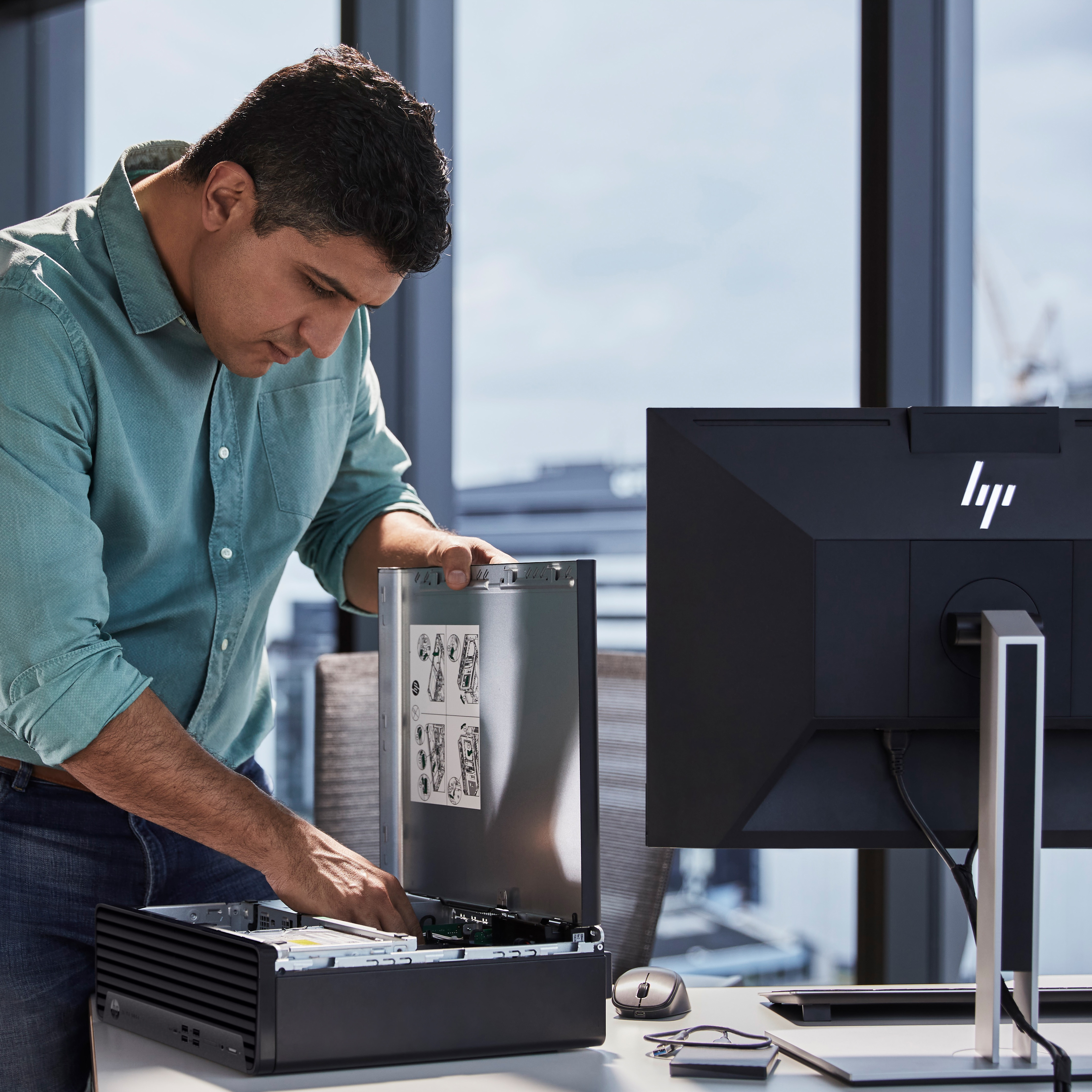 Ein Mann in hellblauem Hemd arbeitet an einem Computer. Er hält ein Computergehäuse. Ein HP-Monitor steht auf einem Schreibtisch.