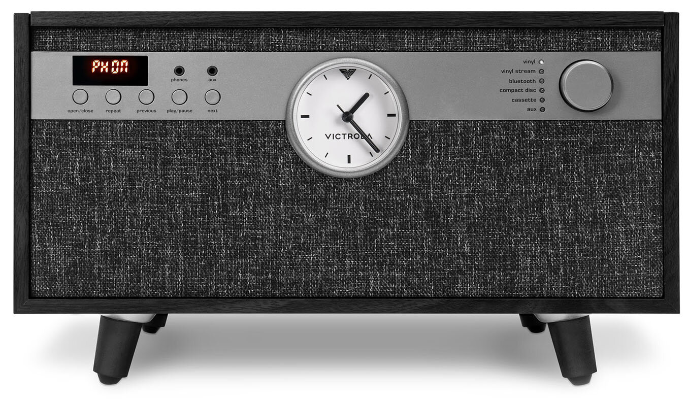 Głośnik Victrola z zegarem, przyciskami i pokrętłem. Ma wyświetlacz z napisem 'PX ON'. Stoi na czarnych nóżkach.