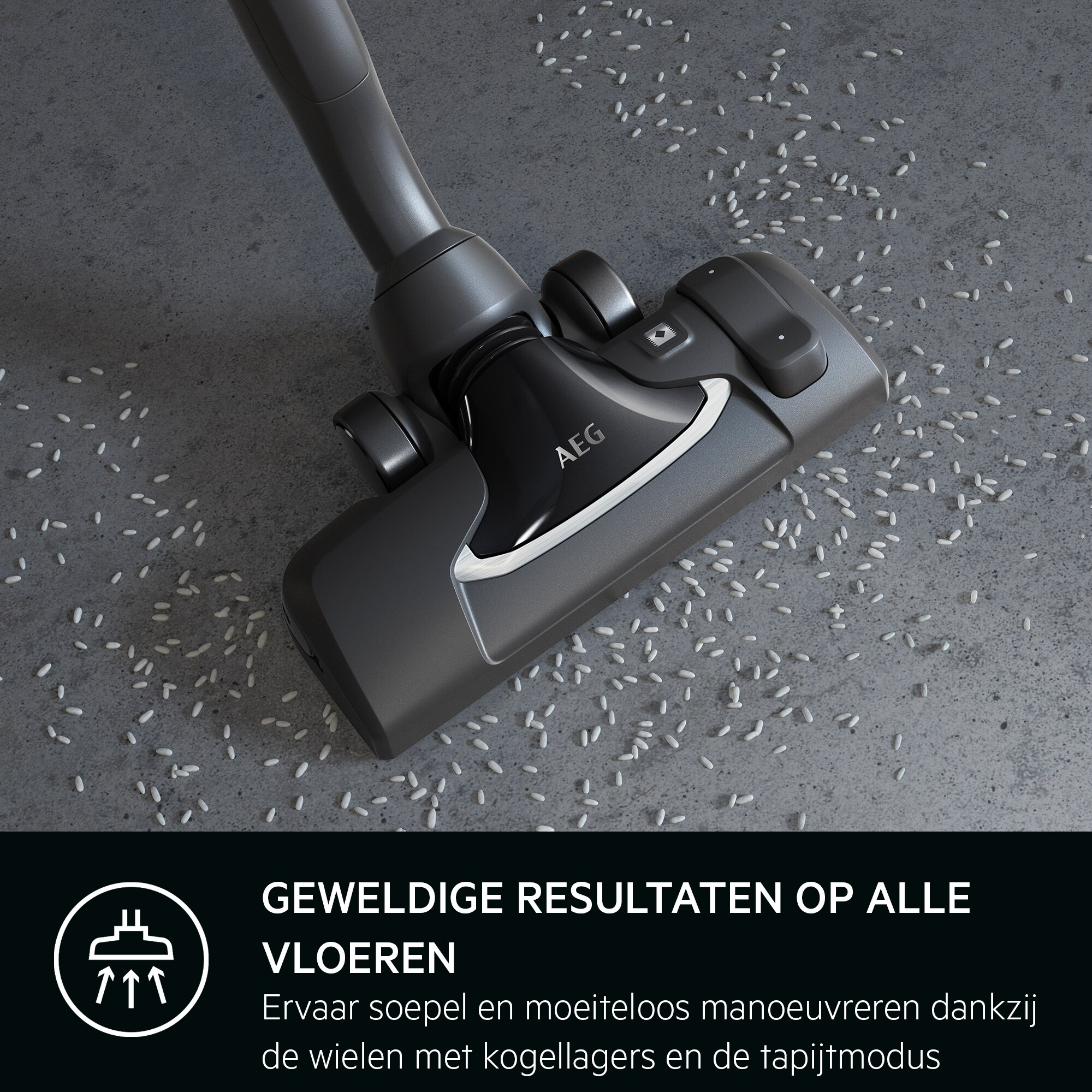 Une tête d'aspirateur gris foncé nettoyant une surface grise parsemée d'objets blancs en forme de riz. Le logo AEG est visible.