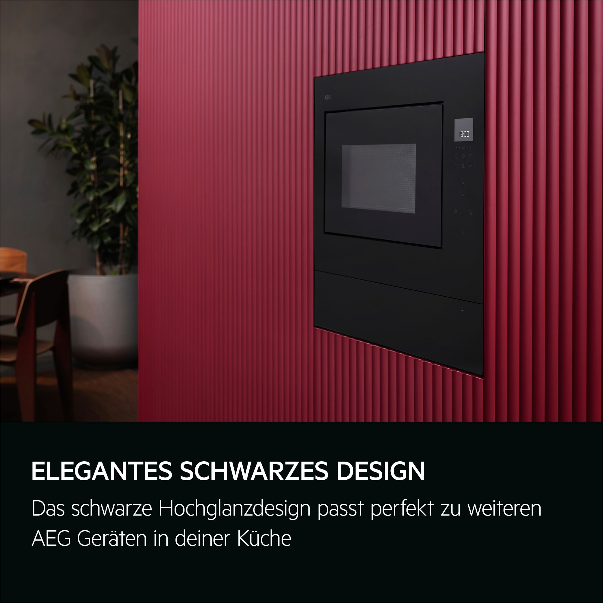 Eine schwarze Mikrowelle ist an einer roten Wand montiert. Links ist eine Pflanze. Die Mikrowelle zeigt die Uhrzeit an.