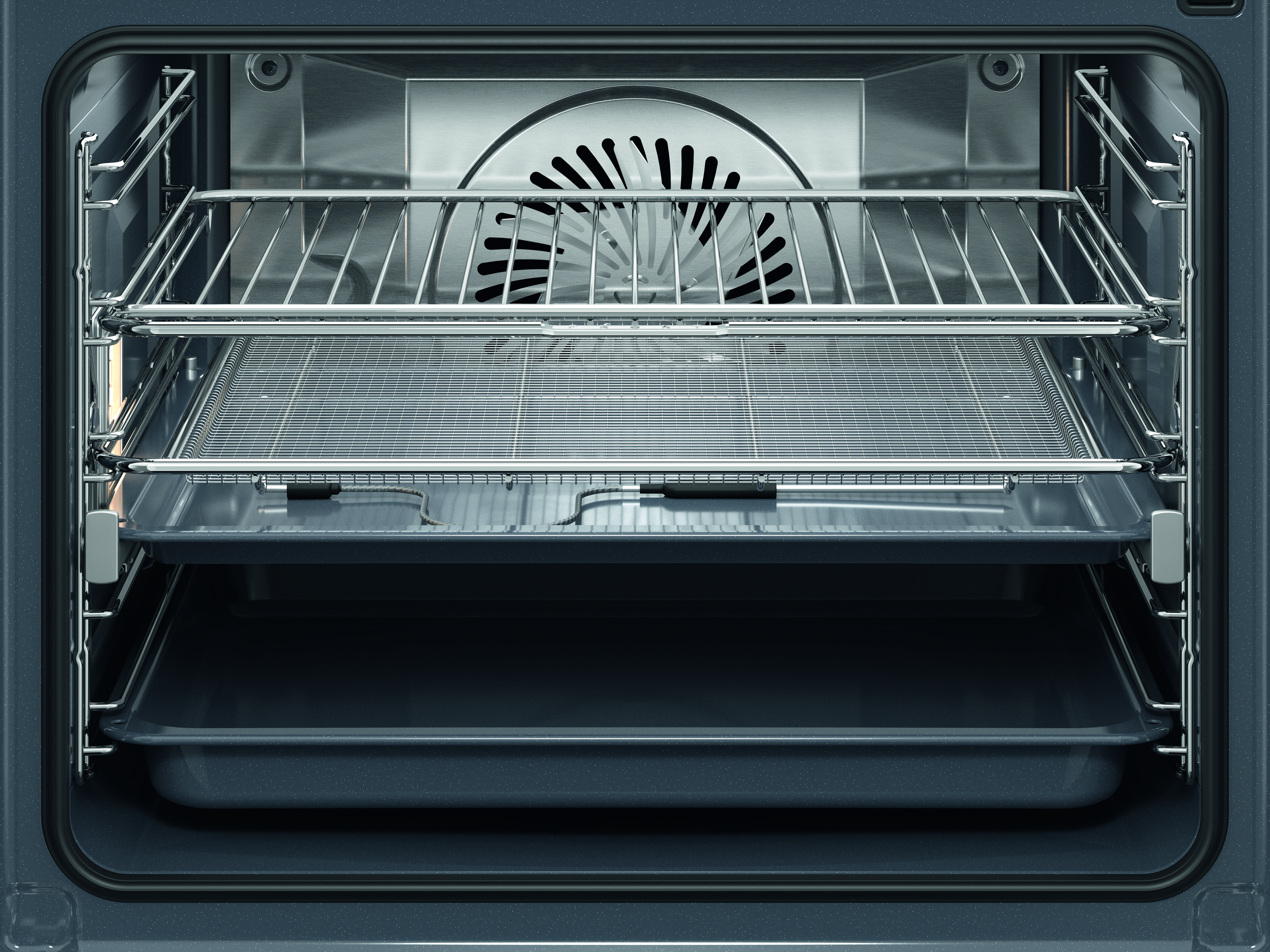 Im Inneren eines Ofens. Es gibt zwei Roste und zwei Tabletts. Hinten ist ein Ventilator zu sehen. Der Ofen ist dunkelgrau.