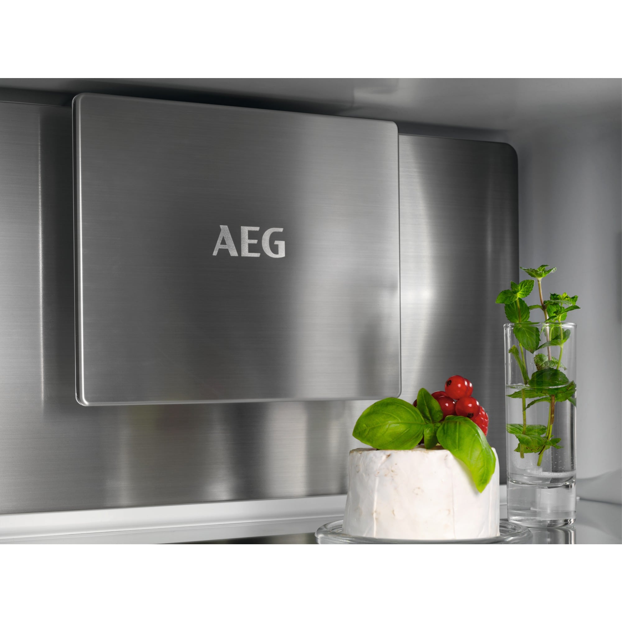 Im Kühlschrank befinden sich Käse mit Beeren und Basilikum im Vordergrund. Ein Glas Minze befindet sich rechts. AEG-Logo links.