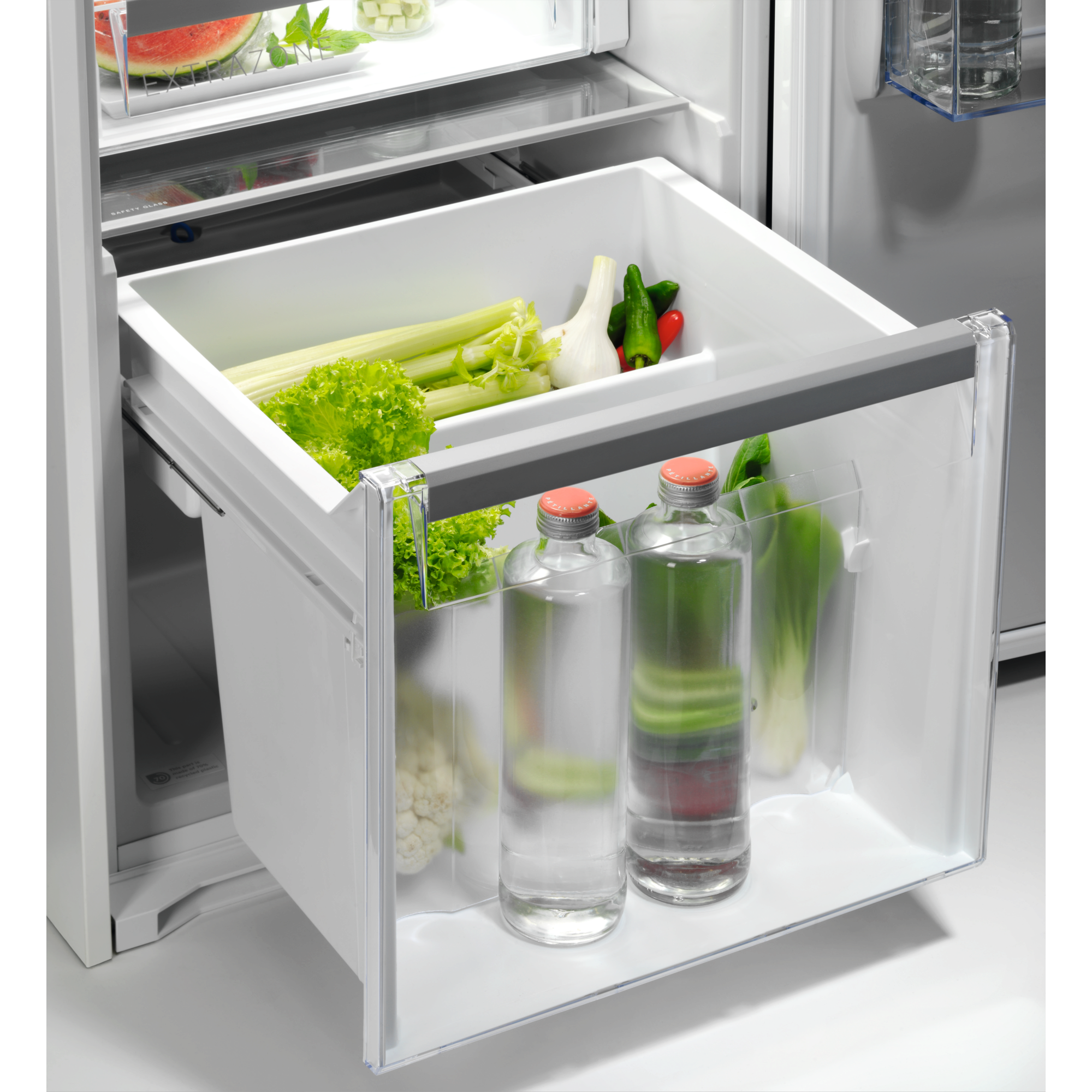 Kühlschublade mit Gemüse und Wasser in Flaschen. Sellerie, Salat, Zwiebeln, Paprika und Blumenkohl sind sichtbar.
