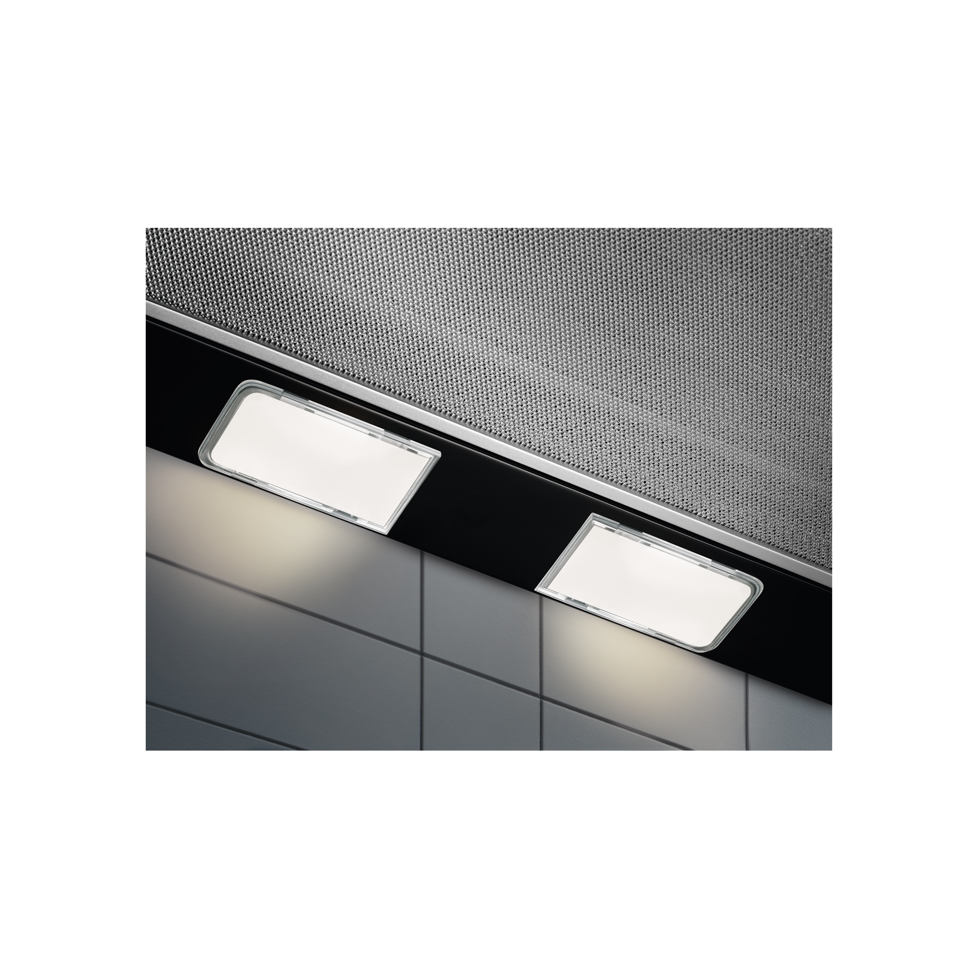 Zbliżenie okapu z dwoma prostokątnymi światłami i metalową siatką. Tłem jest kafelkowa ściana.