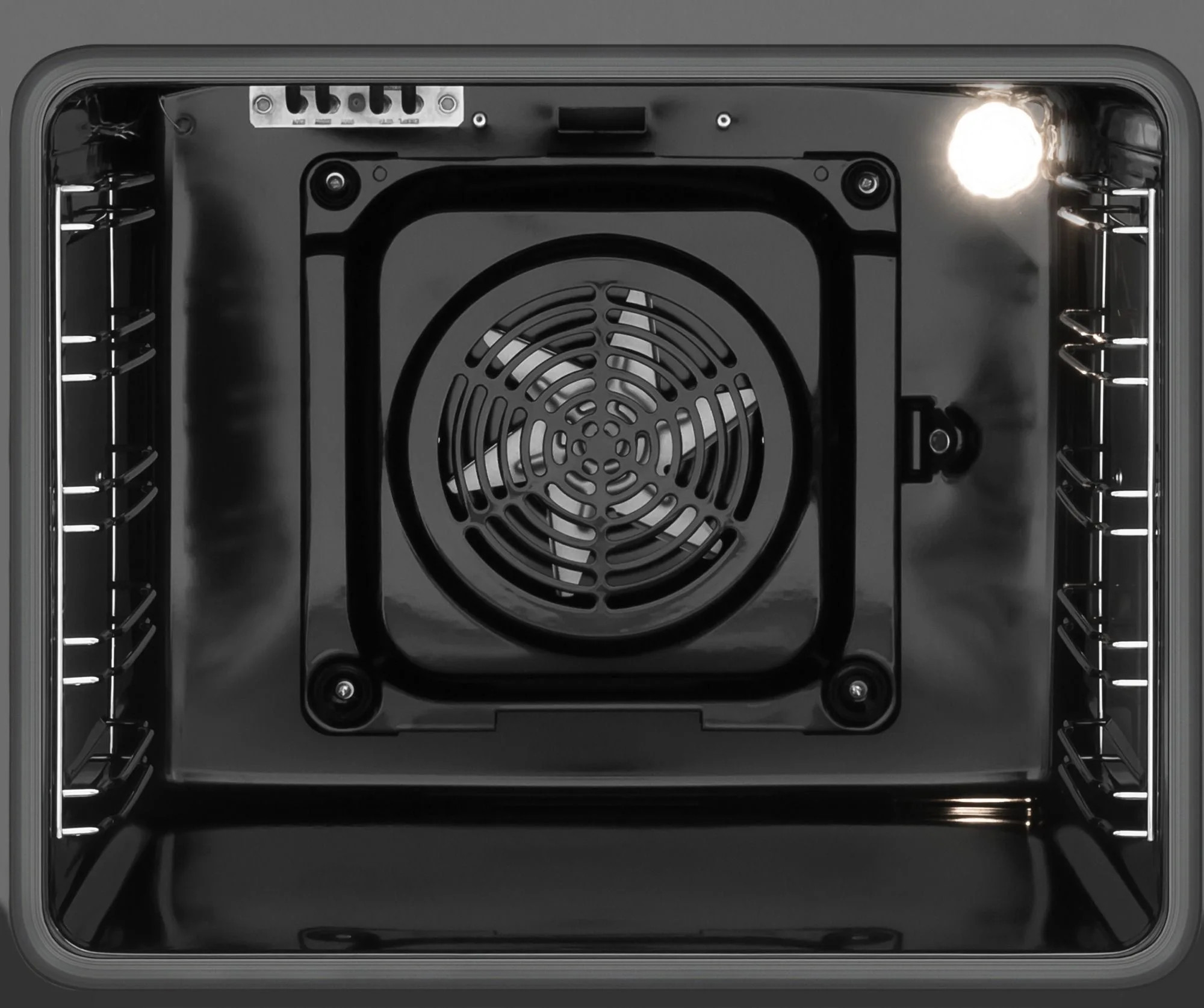 Wnętrze czarnego piekarnika. Widoczny wentylator i światło. Ruszty piekarnika po bokach.