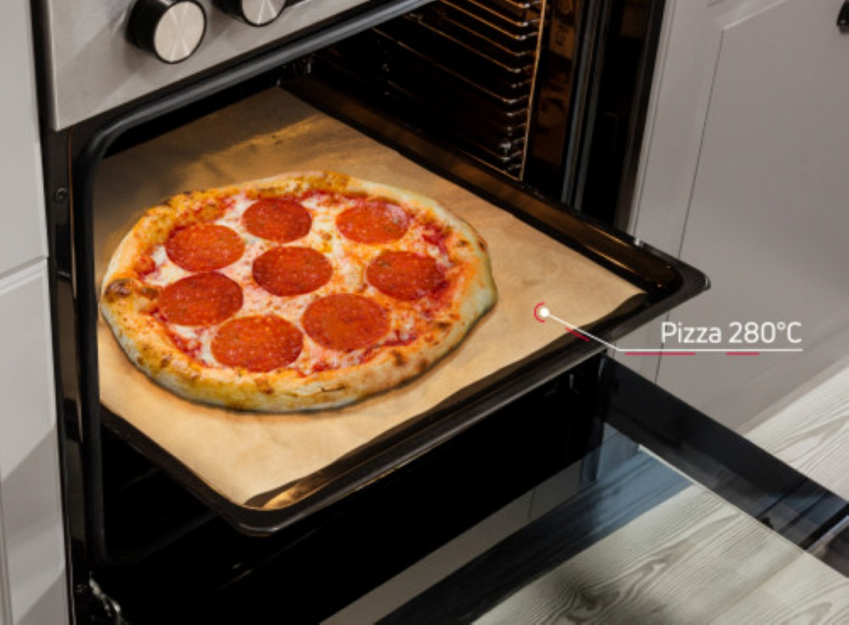 Pizza z pepperoni piecze się w piekarniku. Drzwi piekarnika są otwarte. Pizza jest na tacy.