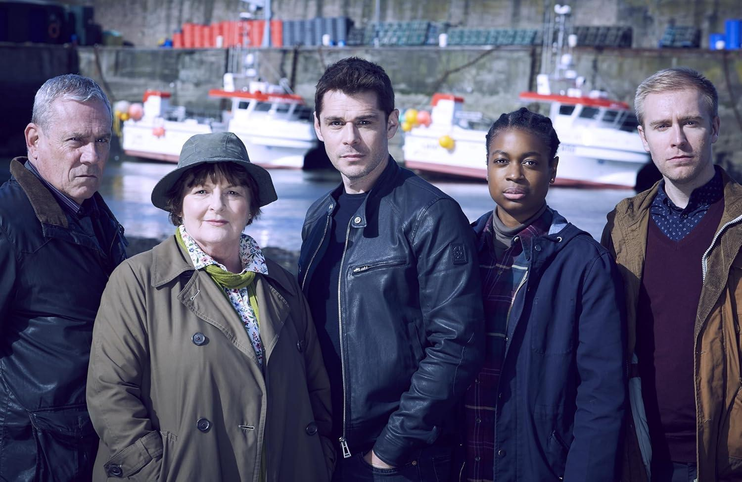 Fünf Personen posieren für ein Foto. Sie stehen vor Booten in einem Hafen. Der Hintergrund umfasst einen Pier und Boote.