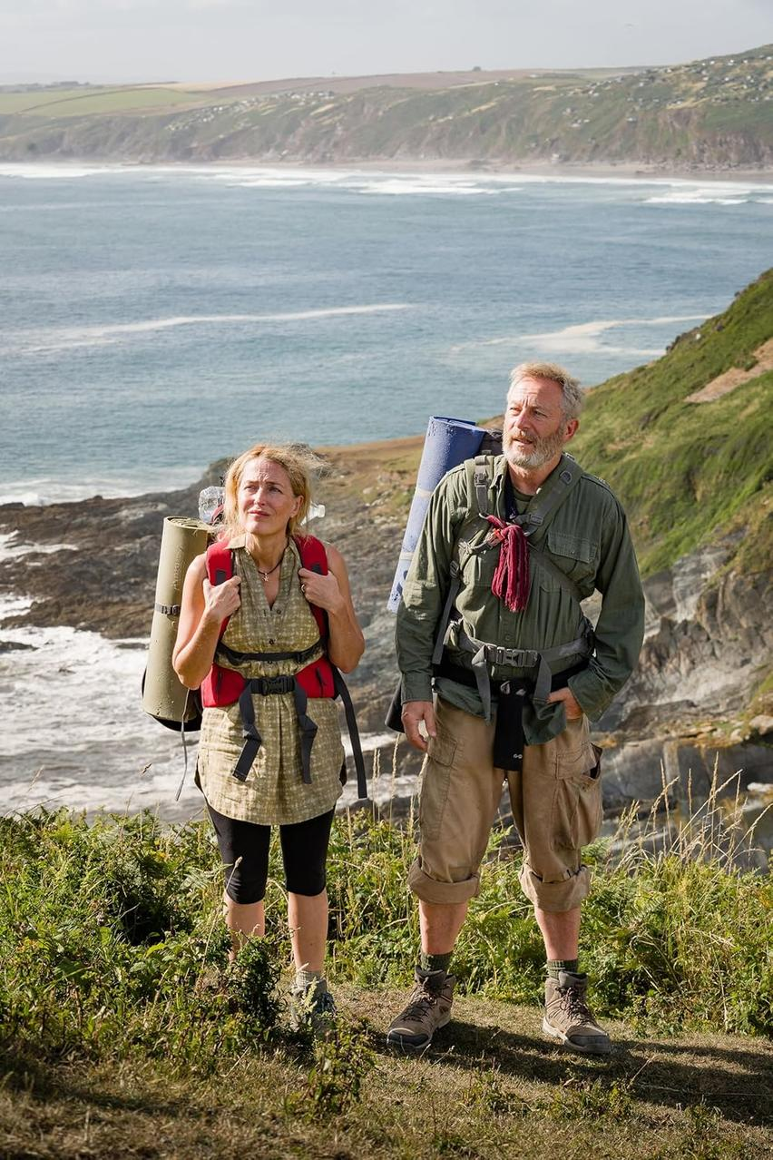 Ein Mann und eine Frau mit Rucksäcken stehen auf einer Klippe mit Blick auf das Meer. Der Mann hat einen Bart. Die Frau hat blonde Haare.
