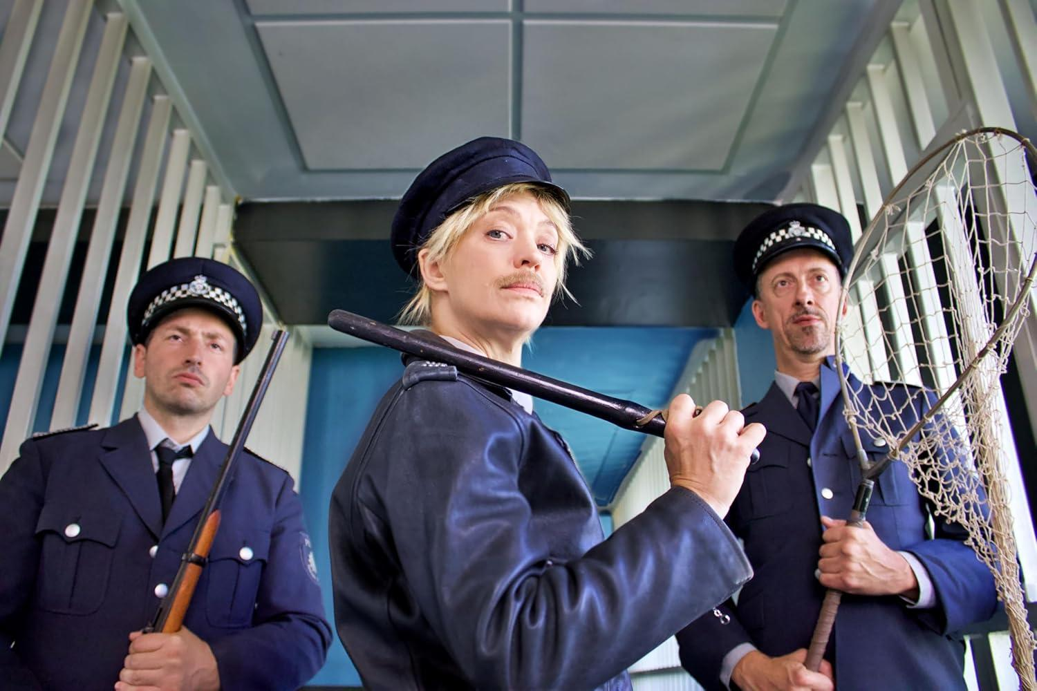 Drei Personen in Polizeiuniformen, eine mit einem Schlagstock, eine andere mit einem Netz und die dritte mit einem Gewehr. Gefängnisgitter im Hintergrund.