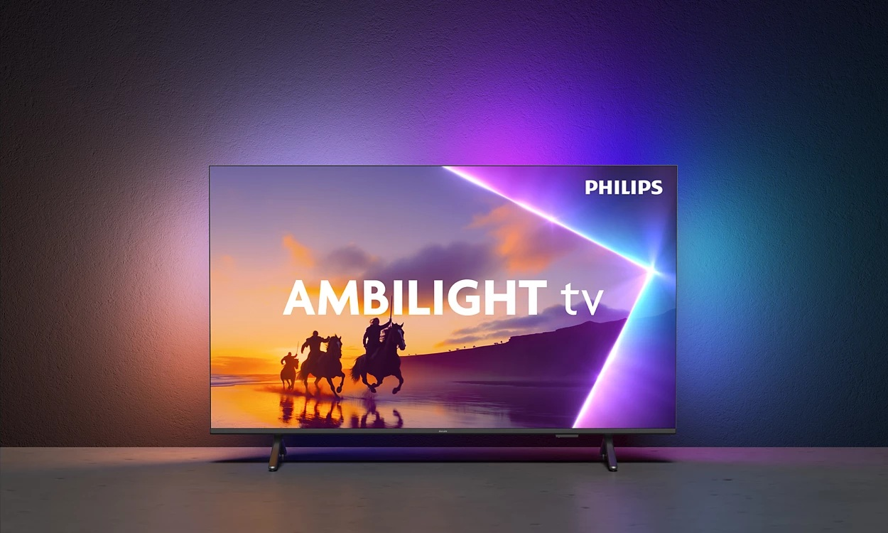 Telewizor Philips Ambilight wyświetla jeźdźców na koniach na tle zachodu słońca. Pokój ma kolorowe oświetlenie ścienne.