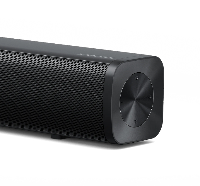 Zbliżenie czarnego soundbaru. Ma siatkowy przód i okrągły panel sterowania z boku. Tło jest białe.