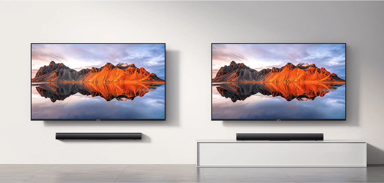 Dwa telewizory wyświetlają górski krajobraz odbijający się w wodzie. Soundbary pod telewizorami. Jeden na ścianie, drugi na szafce.