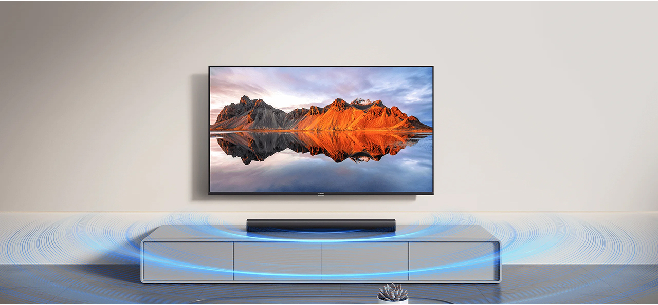 Telewizor na ścianie z soundbarem na szafce. Obraz na TV pokazuje góry odbijające się w wodzie.