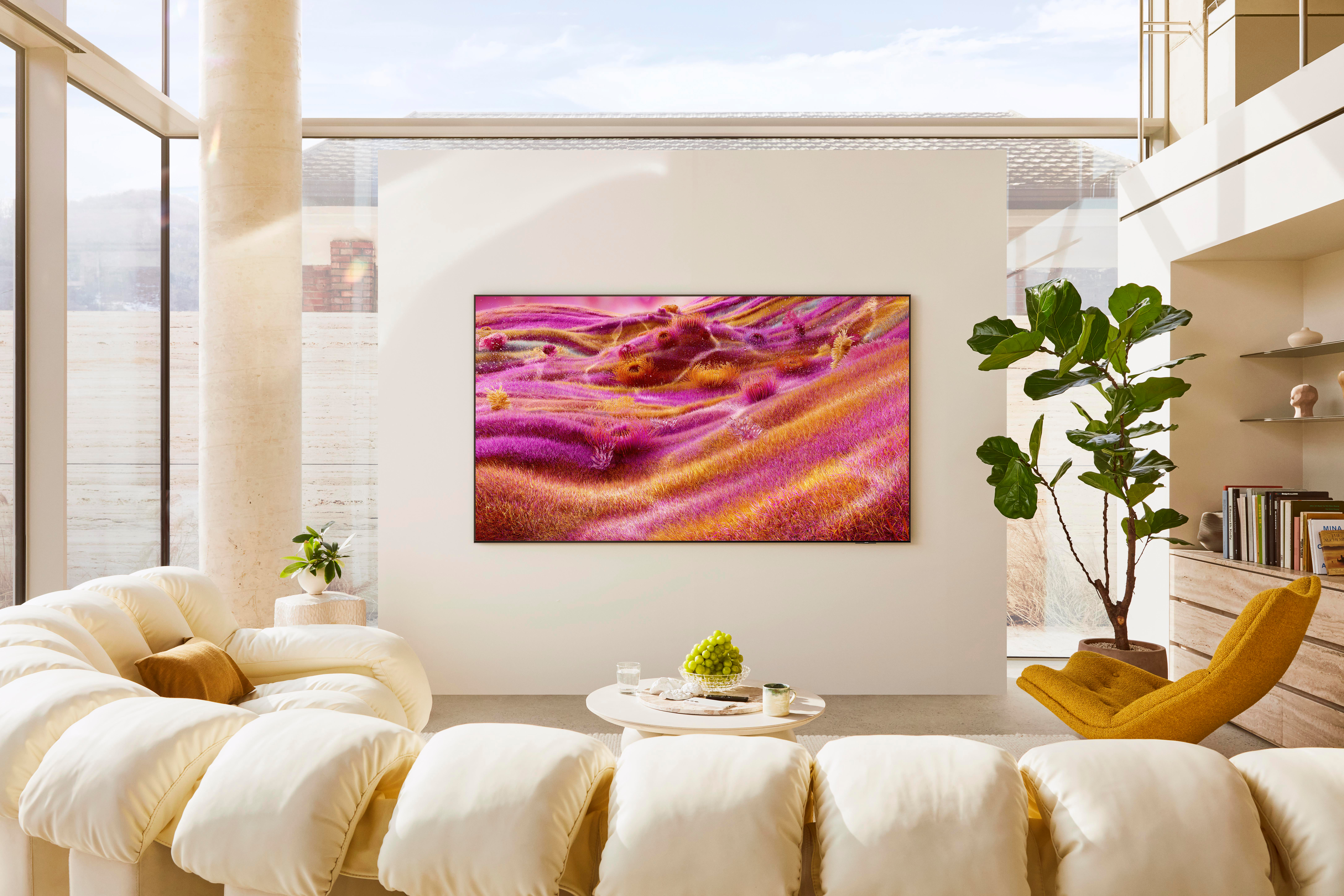 Ein modernes Wohnzimmer mit einem großen Fernseher, der eine abstrakte Landschaft zeigt. Merkmale sind ein cremefarbenes Sofa, ein gelber Stuhl und eine große Pflanze.