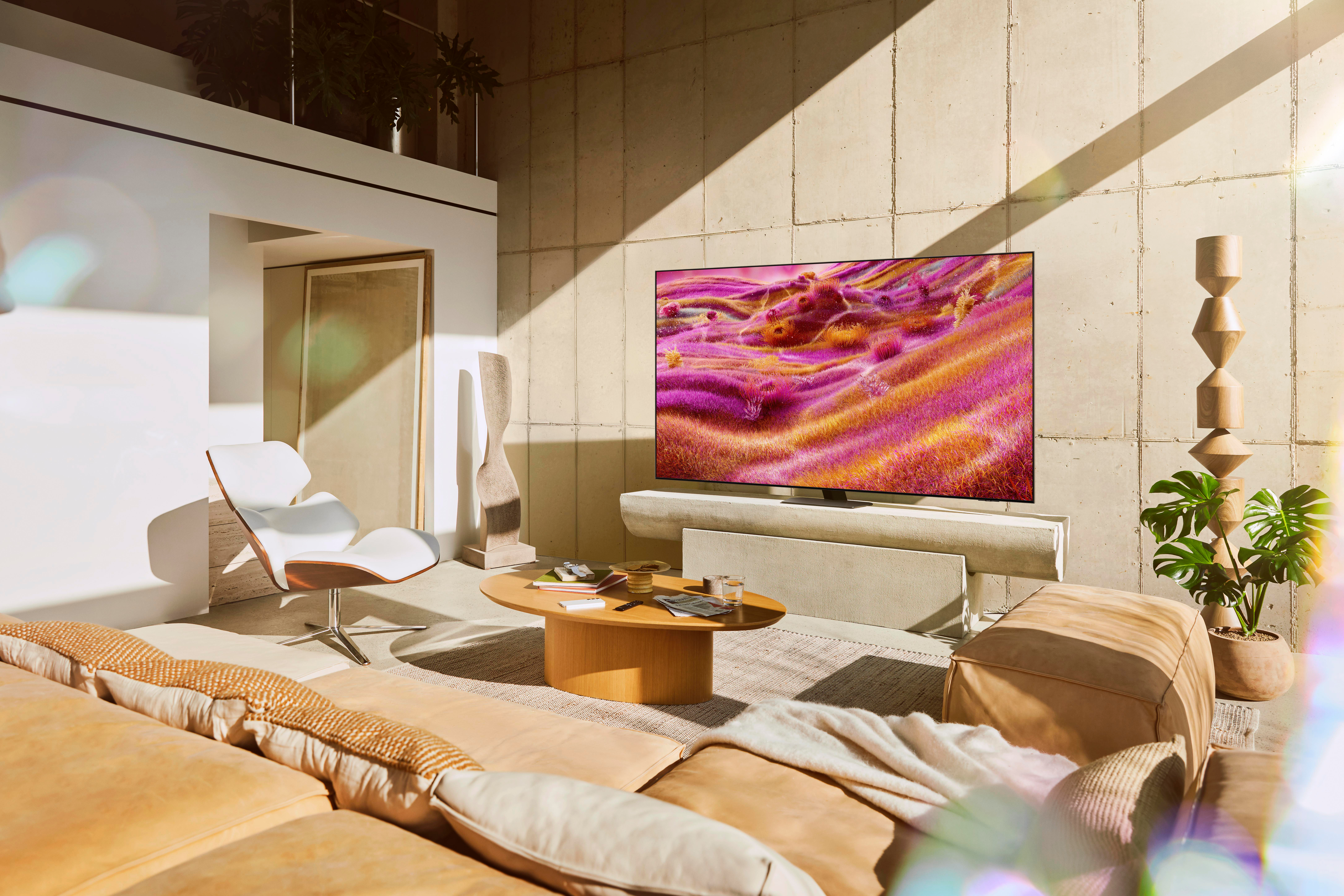 Ein modernes Wohnzimmer mit einem großen Fernseher, der farbenfrohe Kunst zeigt. Eine Couch, ein Stuhl und ein Couchtisch sind im Vordergrund.