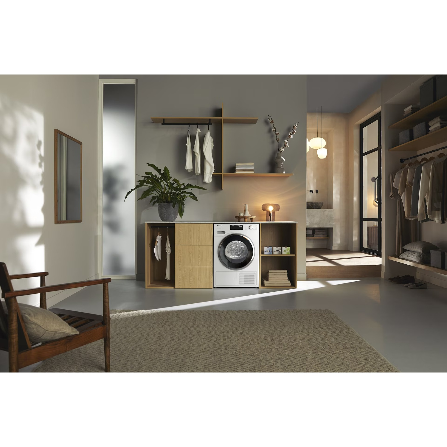 A modern laundry room with a dryer, wooden shelves, a potted plant, a rug, and a wooden chair with a cushion.
