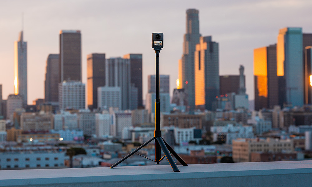 Kamera na statywie z widokiem na panoramę miasta o zachodzie słońca. Budynki odbijają ciepłe światło. Niebo jest zmierzchowe.