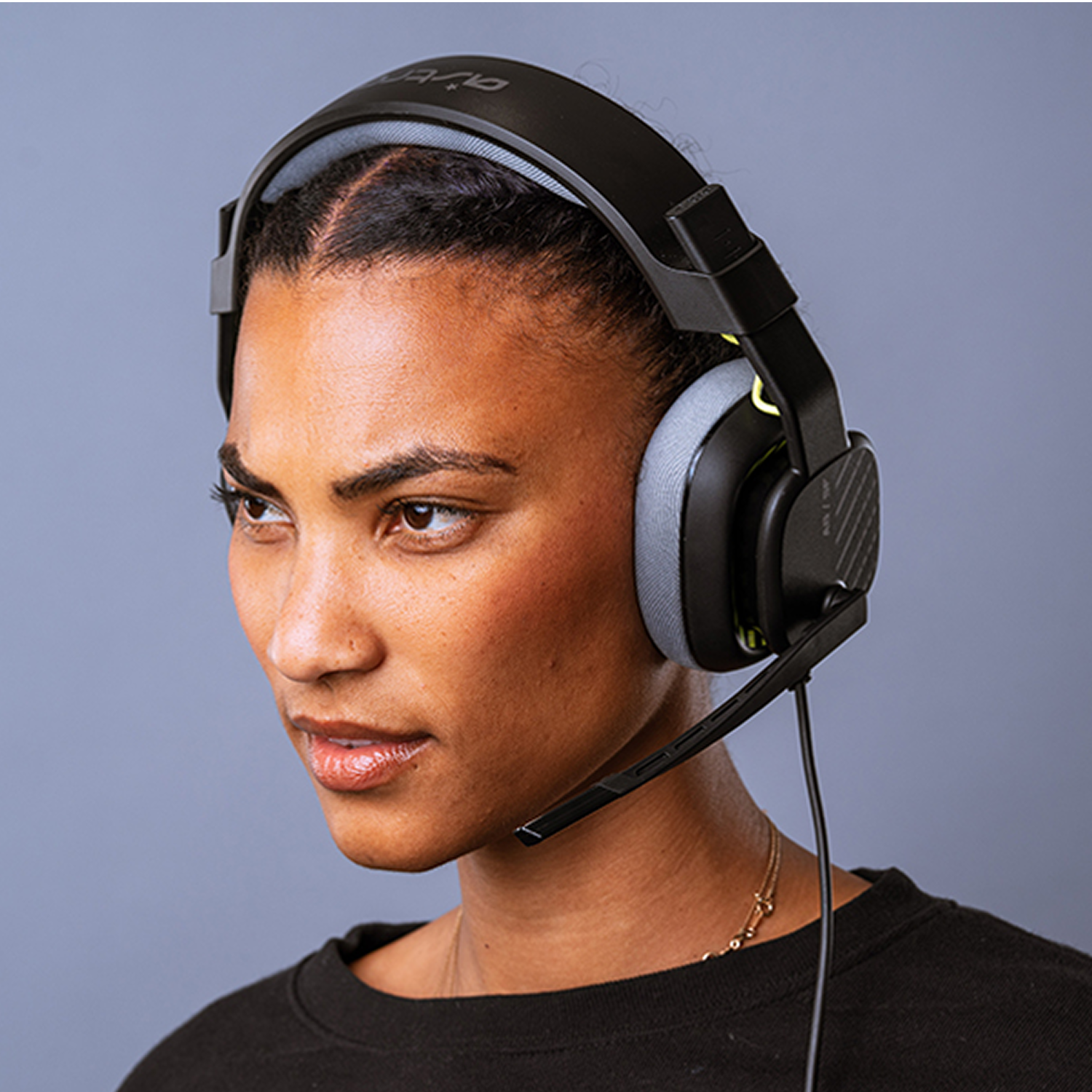 Una mujer con auriculares de juego negros con micrófono, mirando a la izquierda. Tiene una camisa negra y un collar de oro.