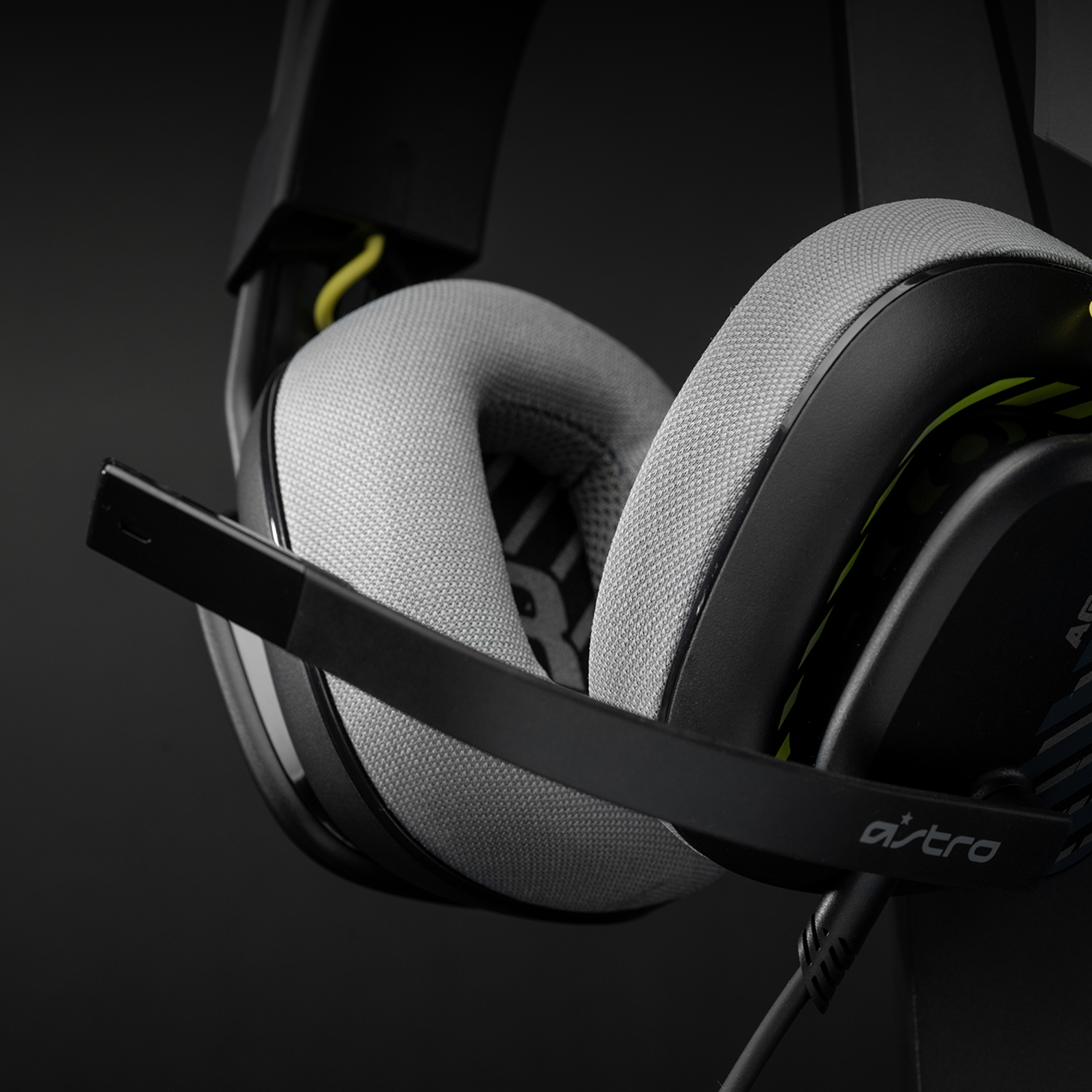 Auriculares para juegos negros con auriculares grises y micrófono, logotipo de Astro visible. Acentos amarillos y fondo oscuro.