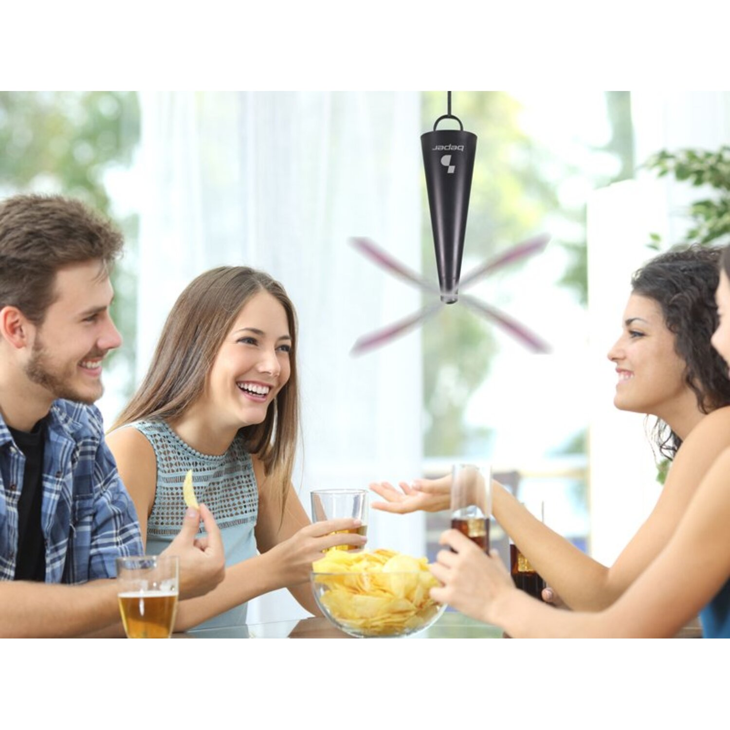 Vier mensen aan een tafel met drankjes en snacks. Een ventilator hangt erboven. Ze lachen en praten.