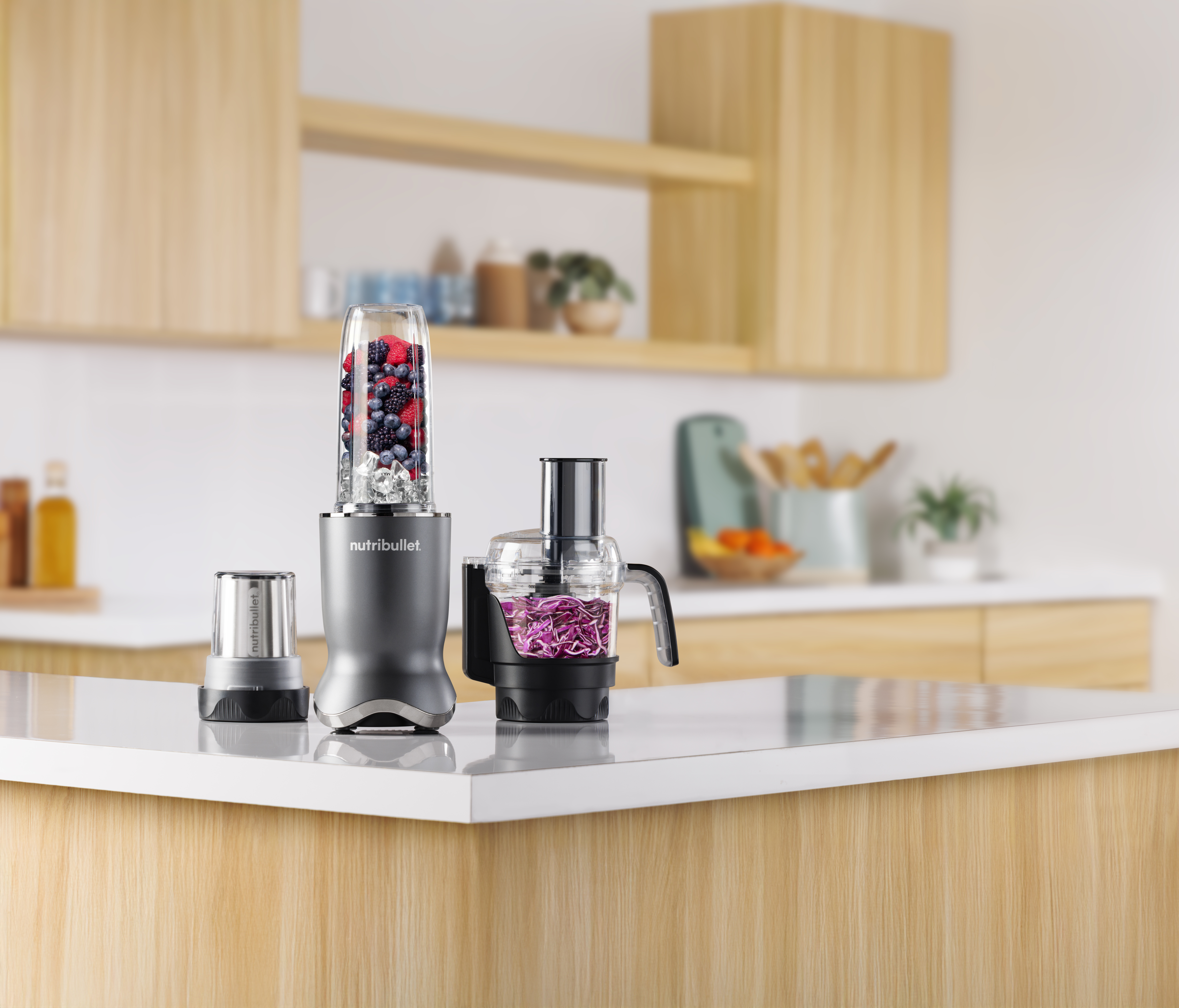 Küchenszene mit einem Mixer voller Beeren, einer Küchenmaschine mit Kohl und einem kleinen Mixbecher.