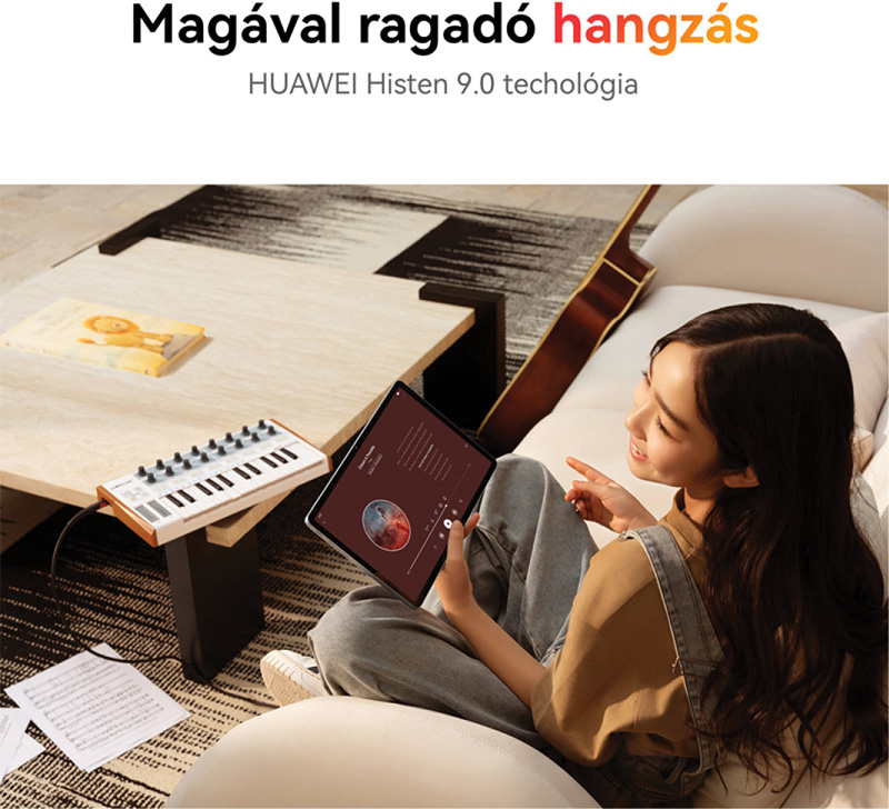 Egy nő a kanapén ül, táblagépet használ. Egy kis billentyűzet és egy könyv az asztalon. Egy gitár a háttérben.