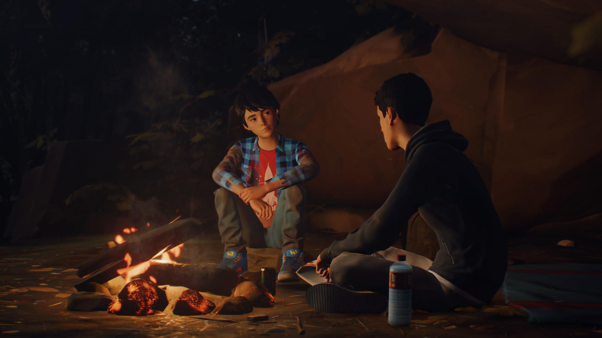 Zwei Personen sitzen am Lagerfeuer. Einer trägt ein blaues kariertes Hemd, der andere einen schwarzen Kapuzenpullover. Brennholz brennt hell. Hintergrund zeigt Zelt und Bäume.