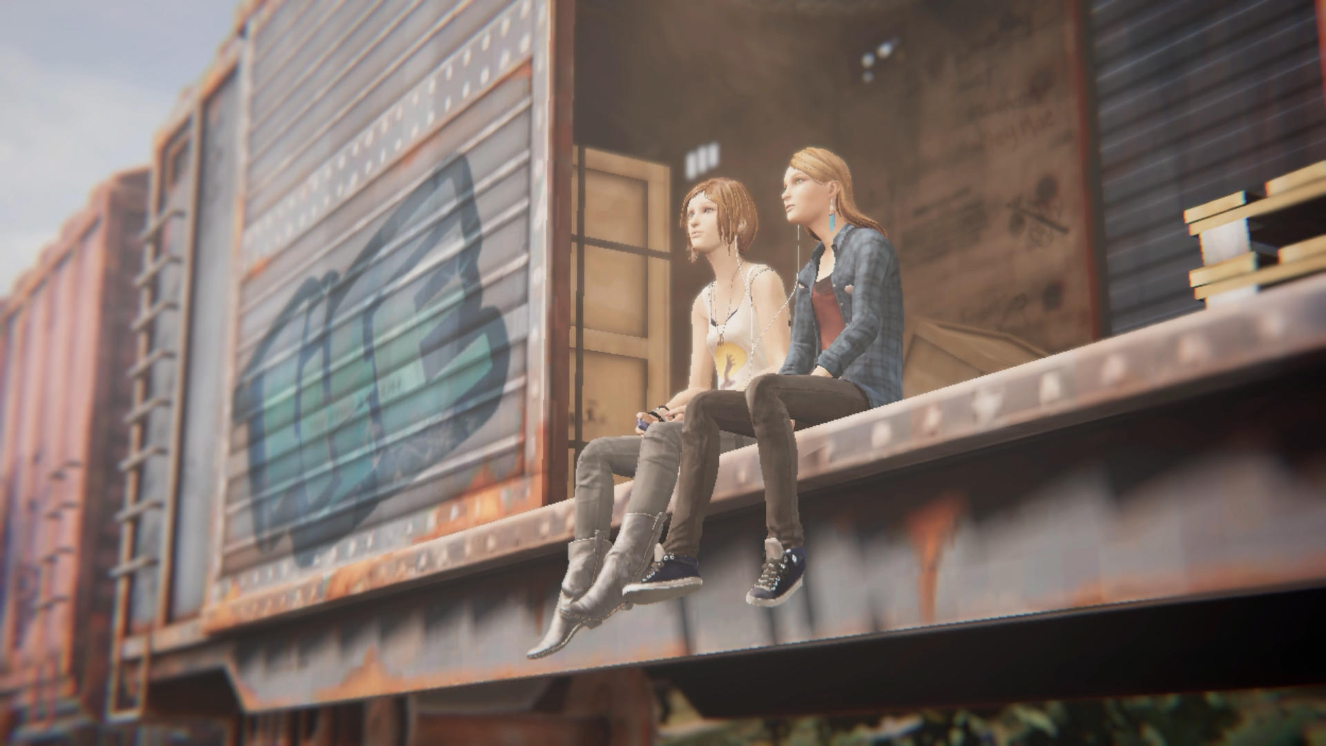 Zwei junge Frauen sitzen auf einem Waggon. Einer trägt ein kariertes Hemd. Graffiti ist auf dem Wagen. Sie schauen hinaus.
