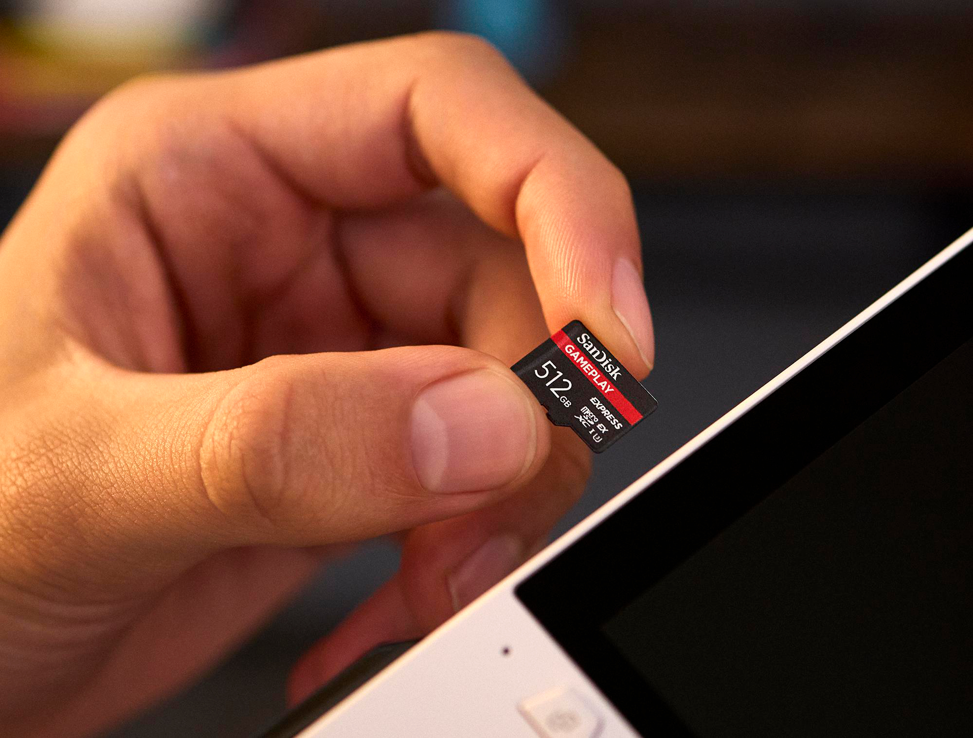 Eine Hand hält eine SanDisk microSD-Karte über einem weißen Gerät. Die Karte ist rot und schwarz. Das Gerät hat einen schwarzen Bildschirm.