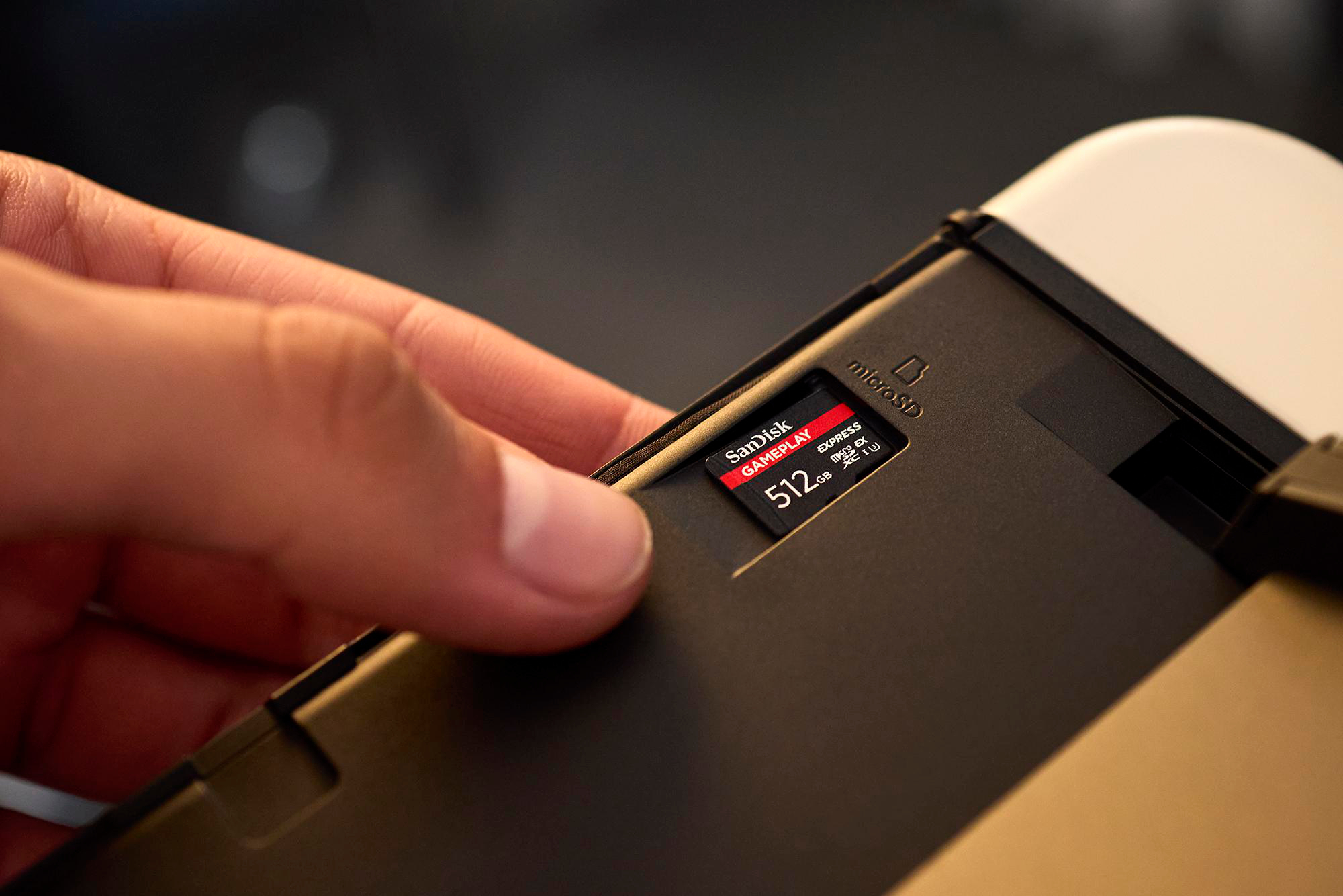 Hand steckt eine 512 GB SanDisk microSD-Karte in ein schwarzes Gerät. Die Karte ist rot und schwarz. Der Hintergrund ist unscharf.
