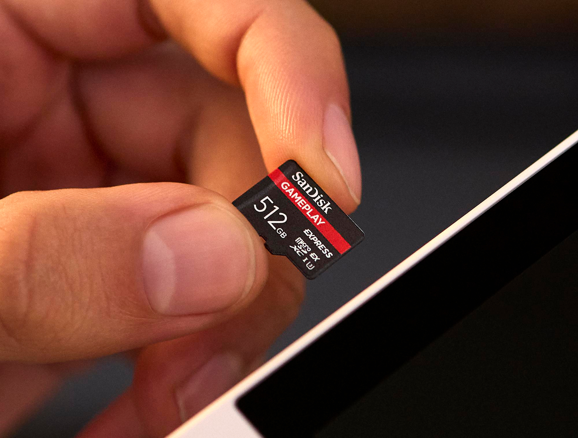 Eine Hand hält eine SanDisk 512GB microSD-Karte. Die Karte ist schwarz und rot. Im Hintergrund befindet sich ein weißes Gerät.