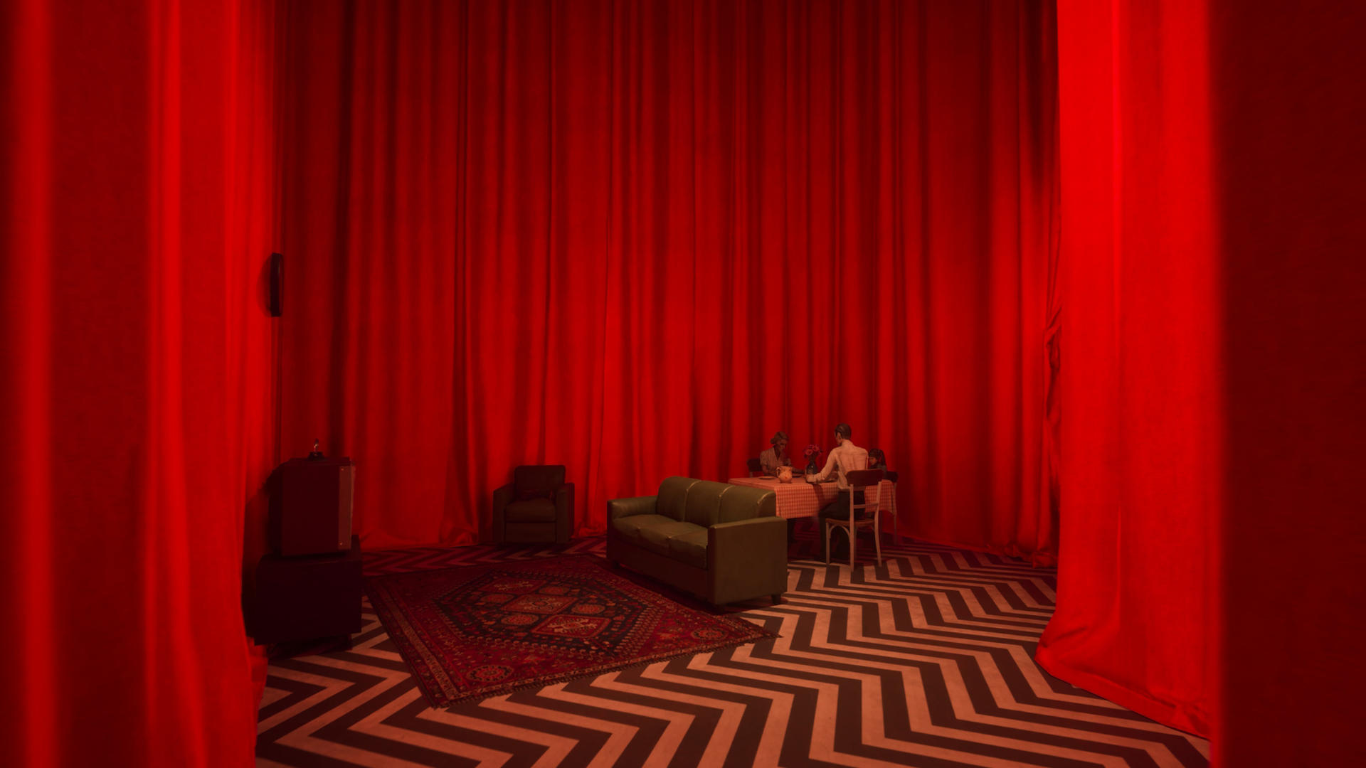 Ein roter Vorhangraum mit schwarz-weißem Zickzackboden. Ein Tisch, ein Sofa und ein Sessel sind vorhanden. Am Tisch sitzen zwei Personen.