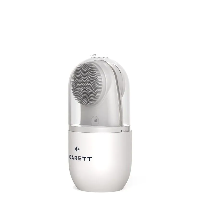 Wyświetlany jest biało-szary pędzel do twarzy firmy Garett. Główka szczoteczki jest szara. Dół jest biały. Góra jest przezroczysta.