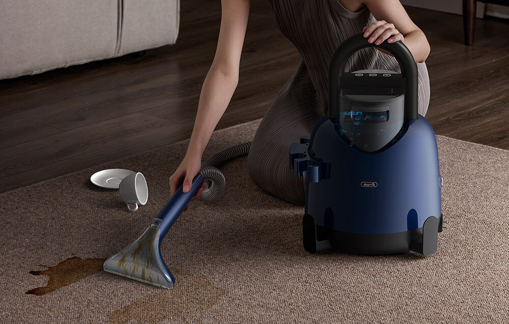 Kobieta czyści plamę na dywanie niebieskim środkiem czyszczącym. W pobliżu rozlana filiżanka kawy. W tle sofa.