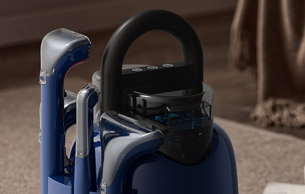 Niebieskie i srebrne urządzenie czyszczące z czarnym uchwytem. Znajduje się na jasnobrązowym dywanie, z rozmytym tłem.