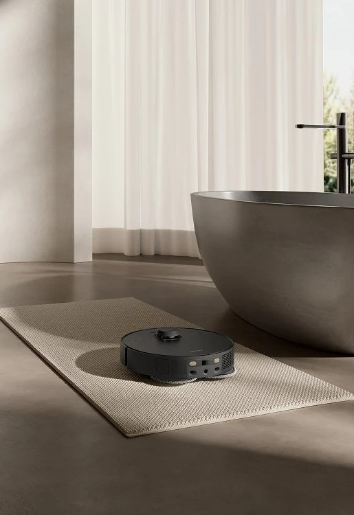 Czarny odkurzacz automatyczny stoi na dywanie w nowoczesnej łazience. Szara wanna i zasłony są w tle.