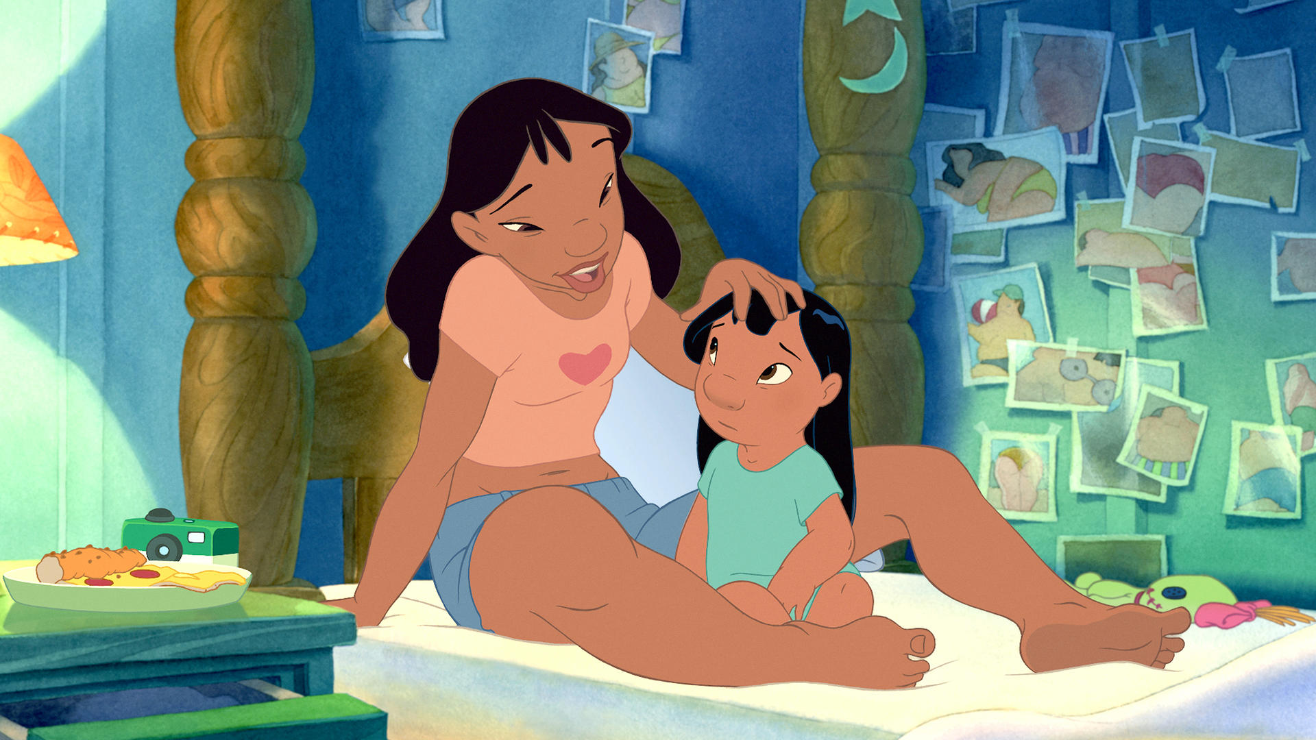 Lilo und Nani aus Lilo und Stitch. Nani berührt Lilos Kopf. Fotos hängen an der Wand. Ein Teller mit Essen und eine Kamera auf dem Tisch.