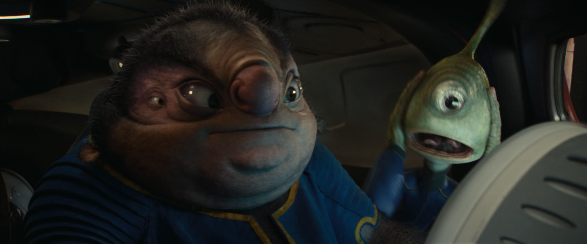 Zwei Aliens in einem Fahrzeug. Einer hat mehrere Augen und eine große Nase, der andere ist grün und überrascht.