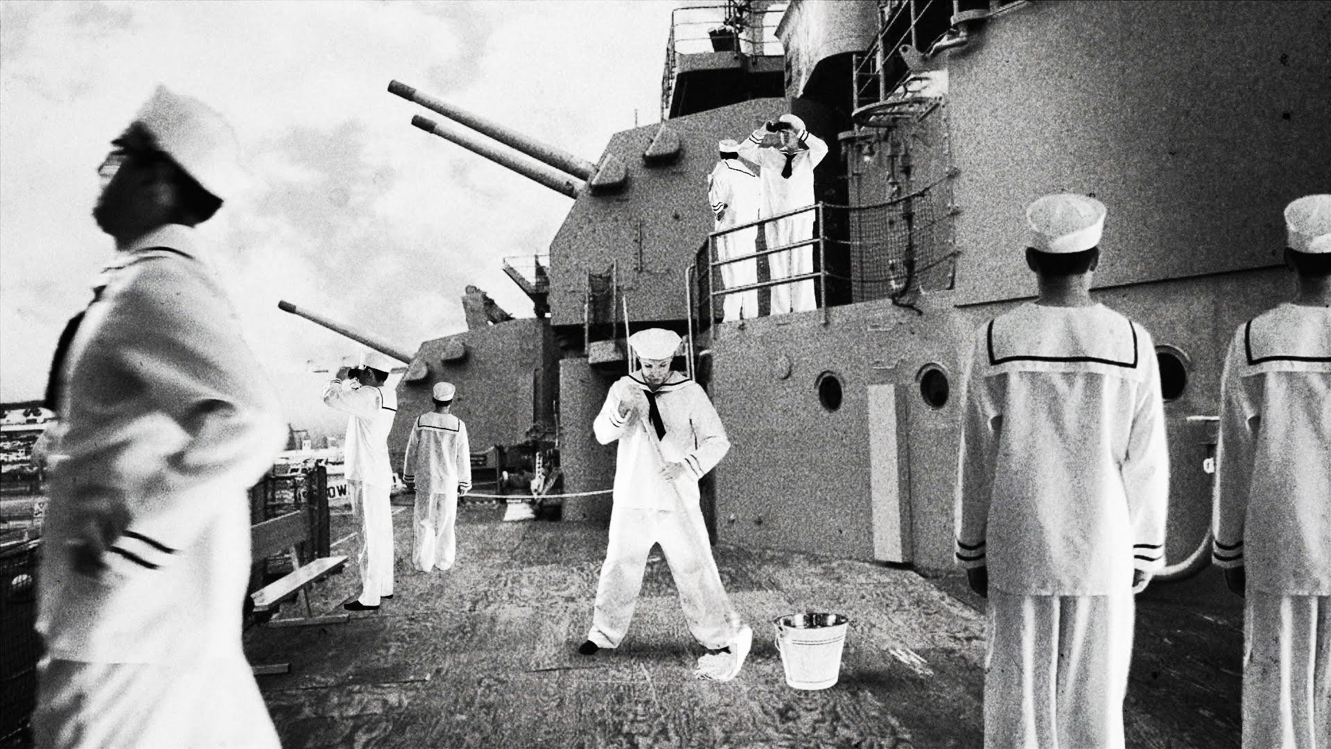 Matrosen in weißen Uniformen auf einem Schiff mit Kanonen.