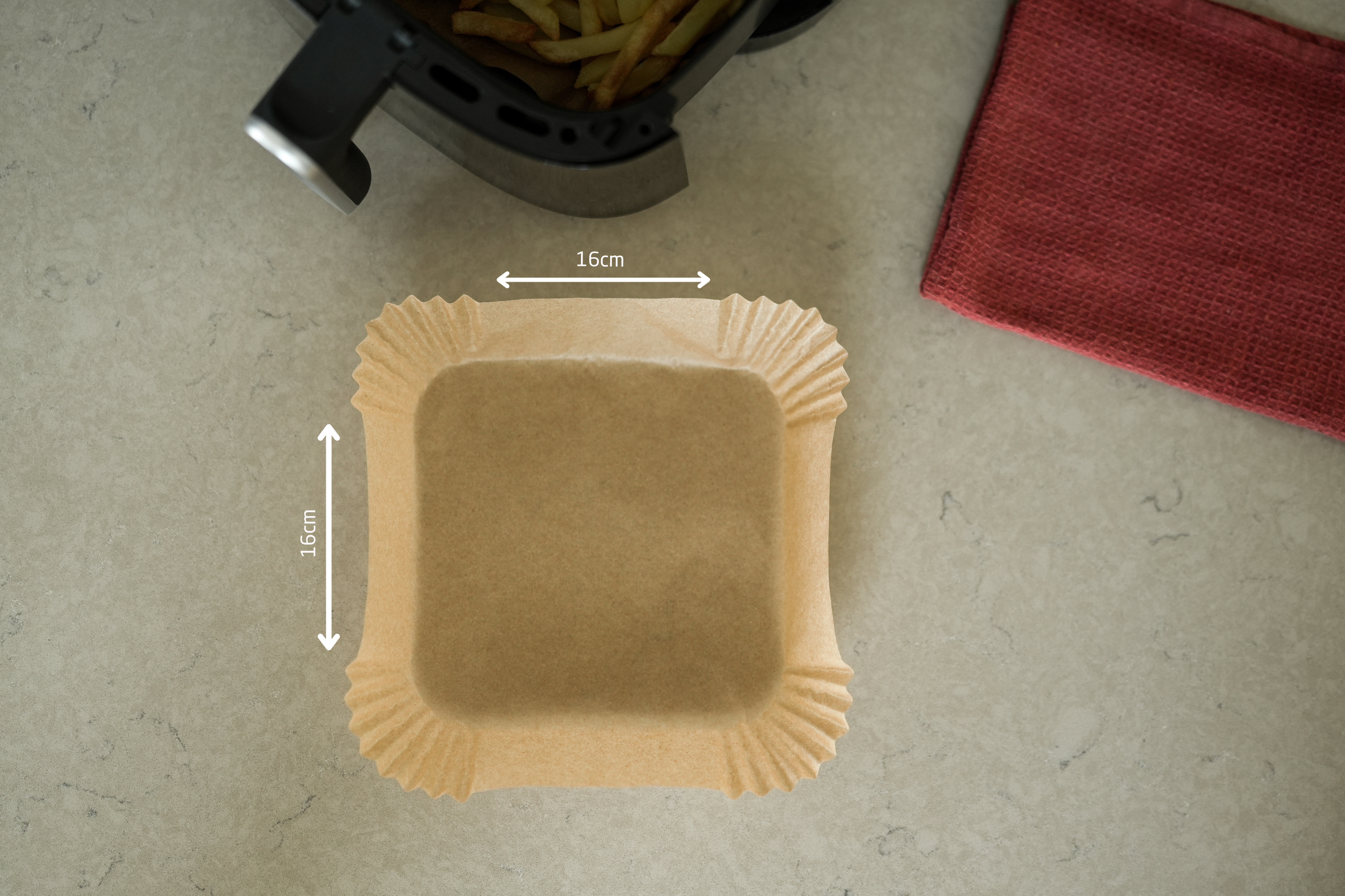 Quadratische Papier-Backform im Airfryer. Rechts ein rotes Handtuch. Abmessungen sind angegeben.