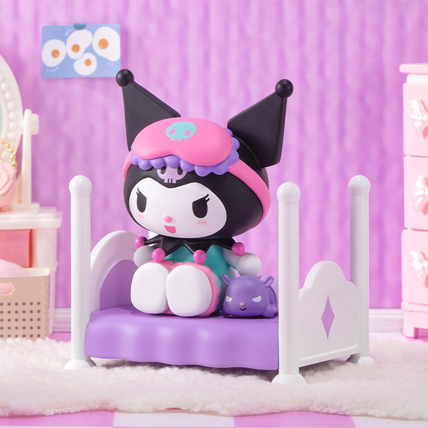 Eine Kuromi-Figur sitzt auf einem lila Bett. Sie trägt eine rosa Augenmaske. Ein kleines lilafarbenes Wesen liegt daneben auf einem weichen, weißen Teppich.