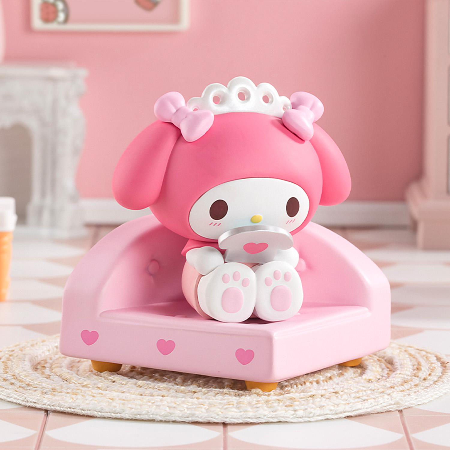 Eine rosa My Melody-Figur sitzt auf einem rosa Sofa mit Herzdetails. Der Hintergrund umfasst eine rosa Wand und einen Teppich.