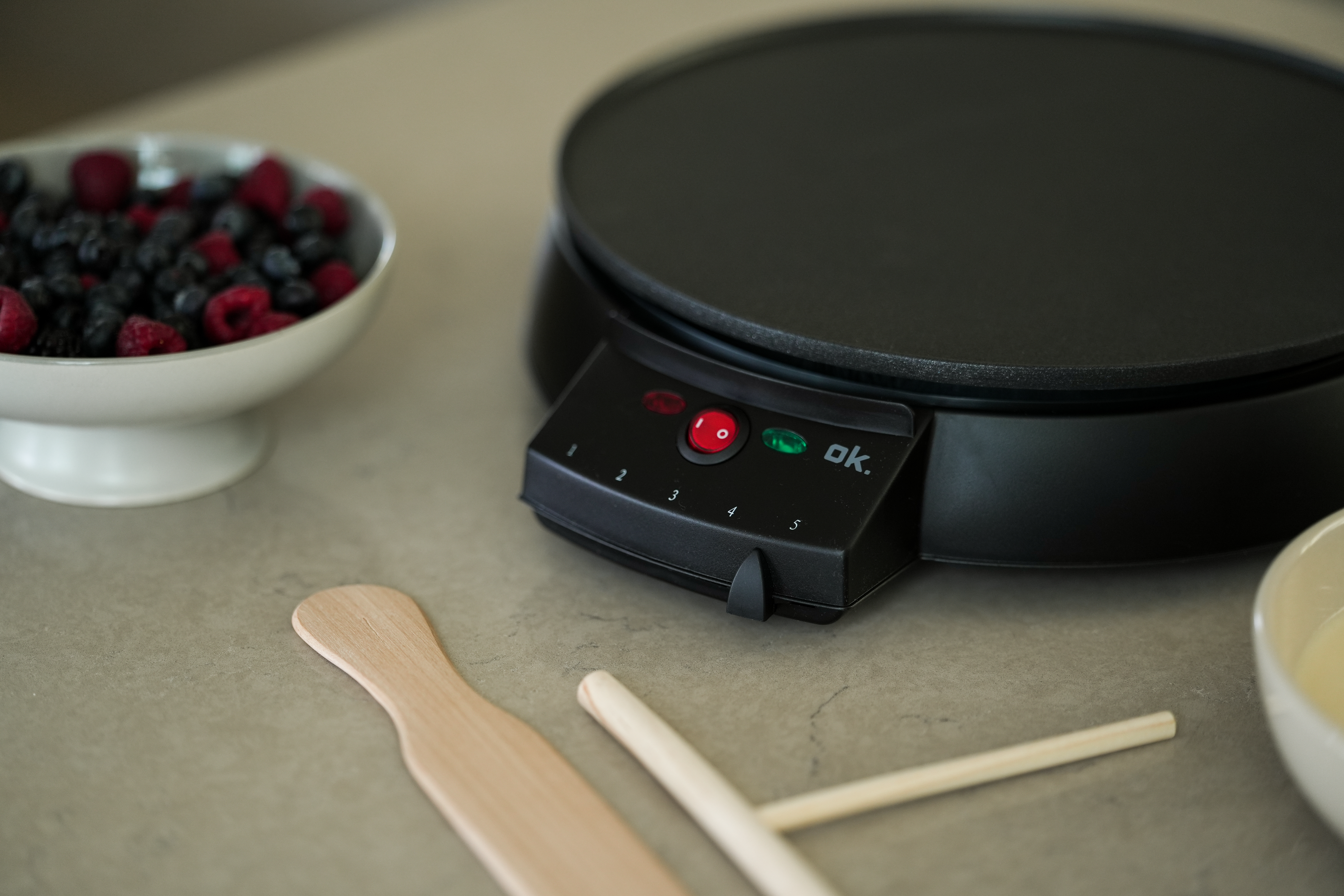 Ein Crêpes-Maker mit einer Schüssel Beeren, Holzutensilien und einer Schüssel mit Flüssigkeit.