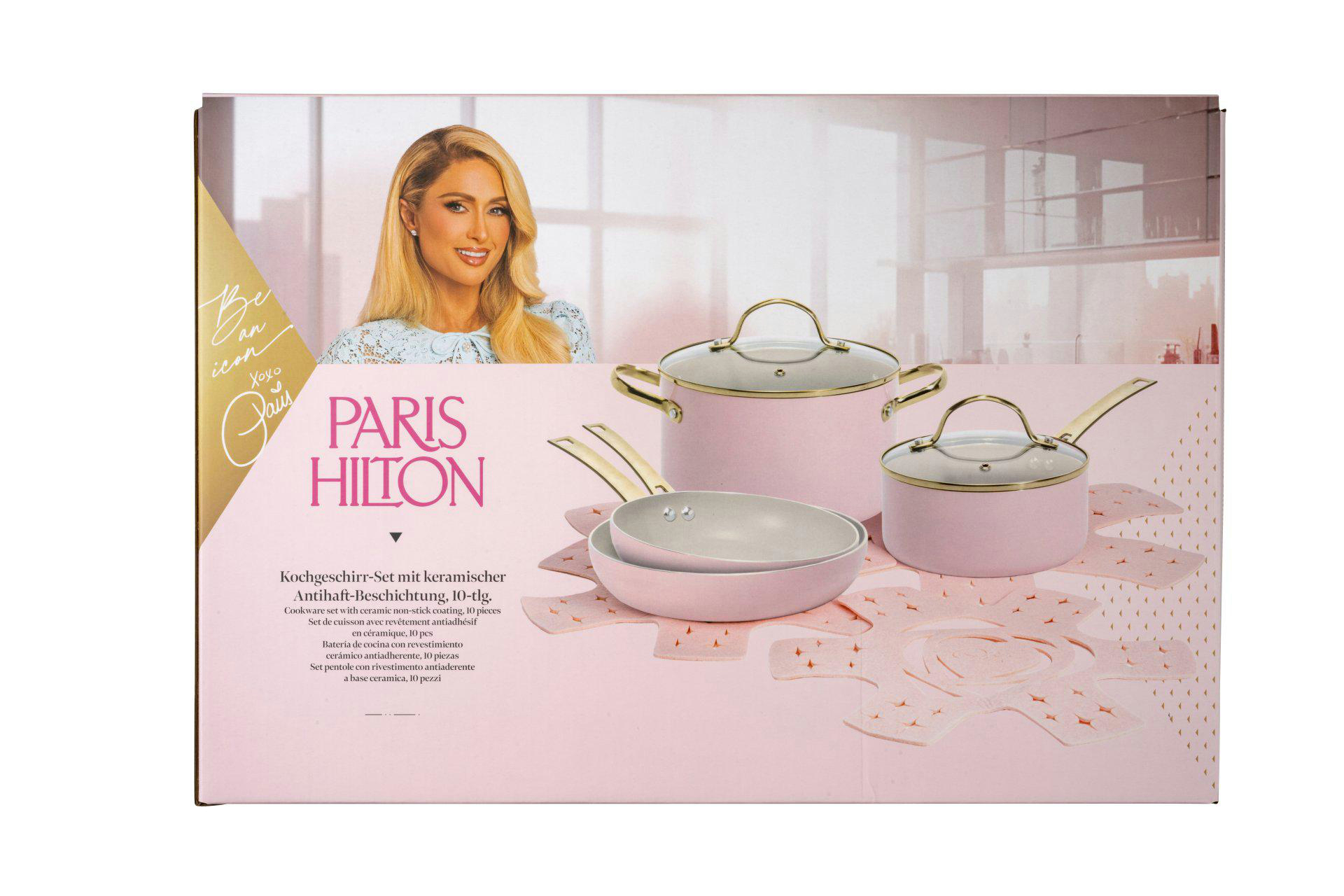 Paris Hilton Kochgeschirr-Set. Rosa Töpfe und Pfannen mit goldenen Griffen werden auf einer rosa Oberfläche gezeigt. Paris Hiltons Bild ist im Hintergrund.