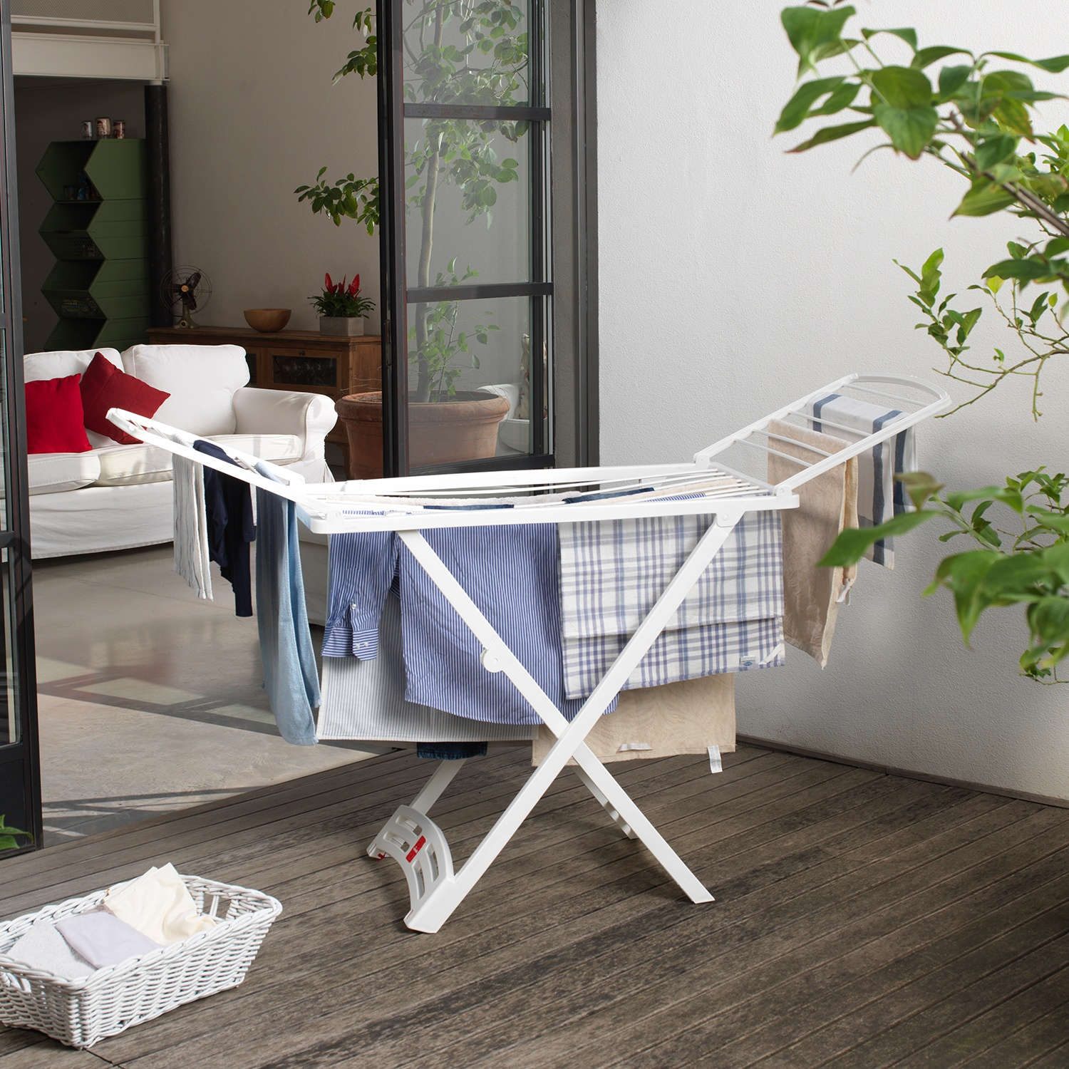 Un stendino bianco con vestiti è su un ponte di legno. Un cesto bianco con vestiti piegati è sul ponte.