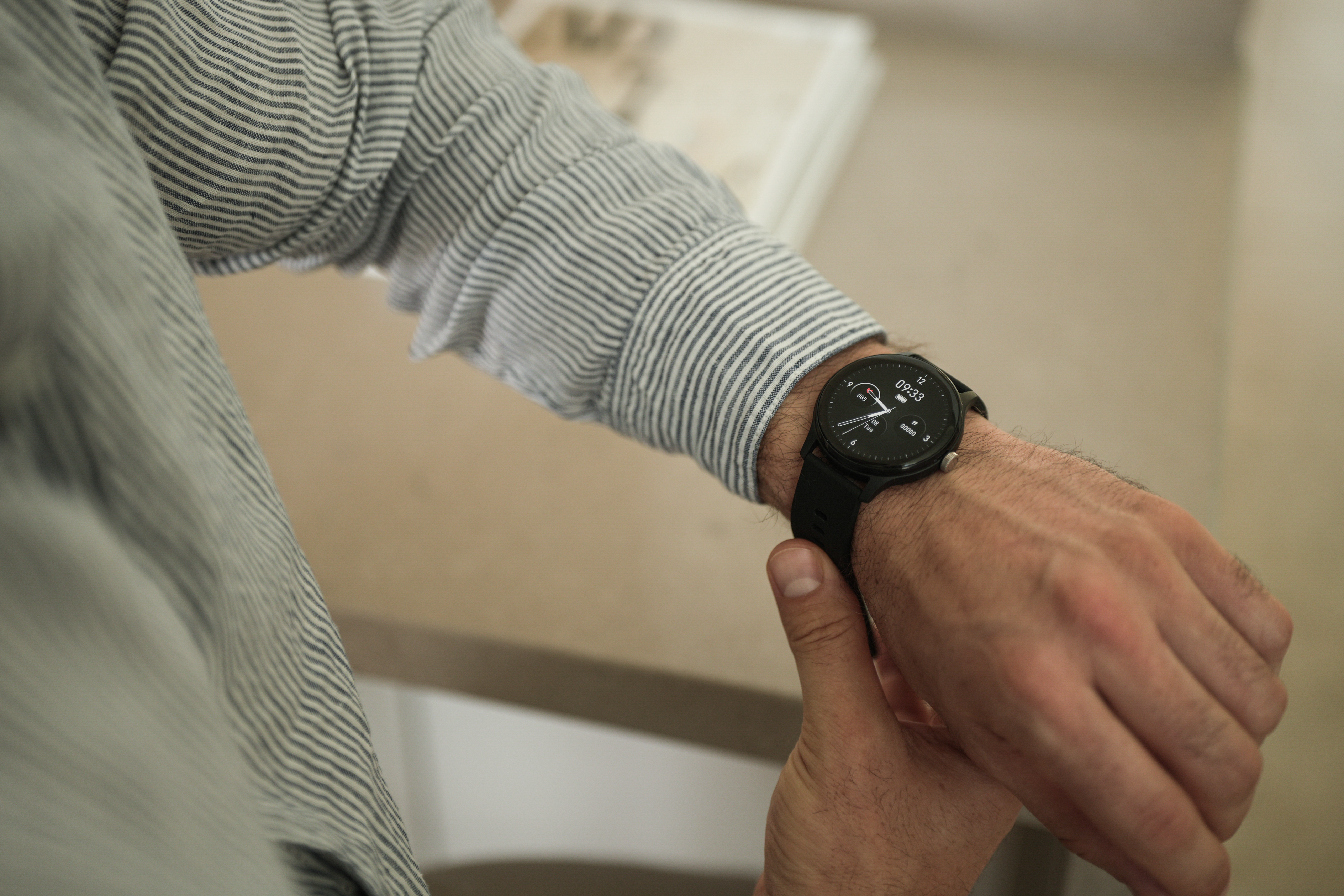 Eine Person in gestreiftem Hemd schaut auf die Smartwatch. Die Uhr zeigt 09:33 Uhr an.
