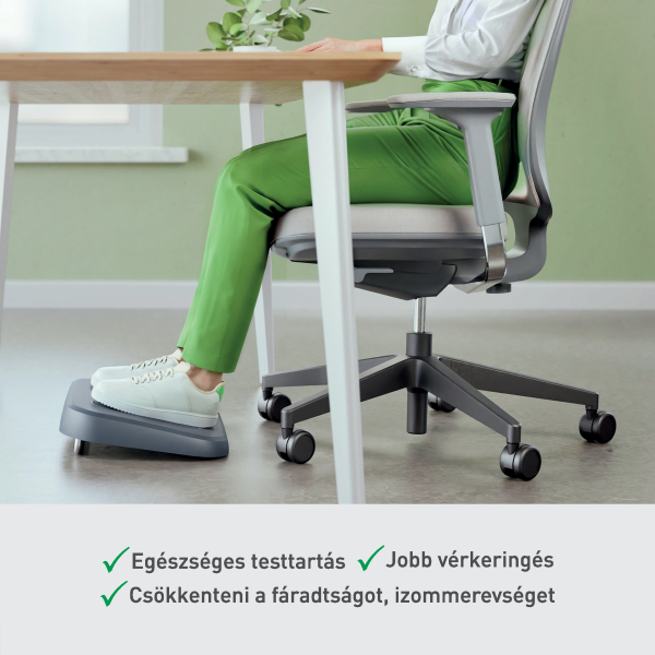 Egy személy az asztalnál ül, lábai a lábtartón. Zöld nadrágot és fehér cipőt visel. Szék és asztal látható.