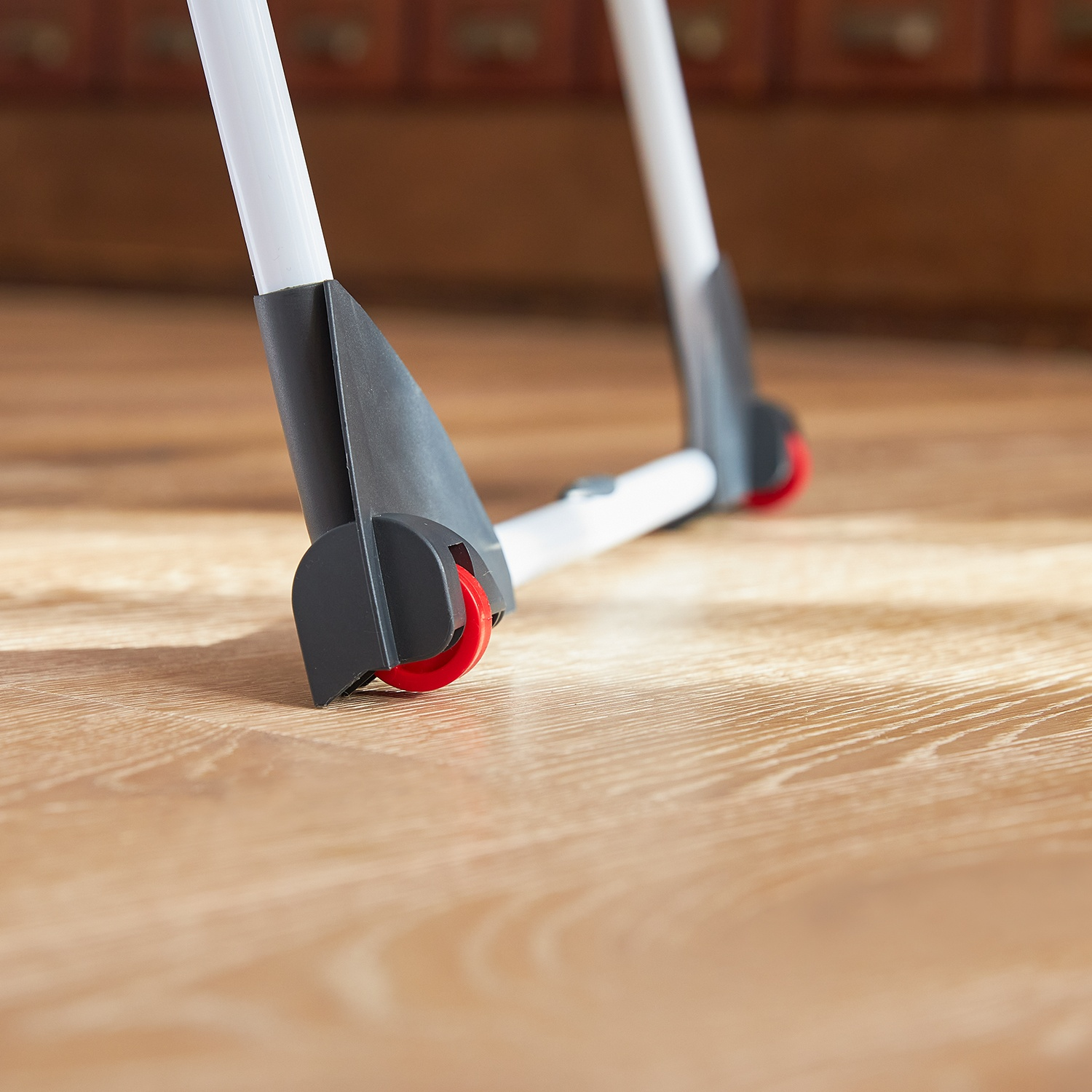 Struttura con ruote bianca e nera su pavimento in legno. Ruote rosse. Mobile in legno marrone sullo sfondo.